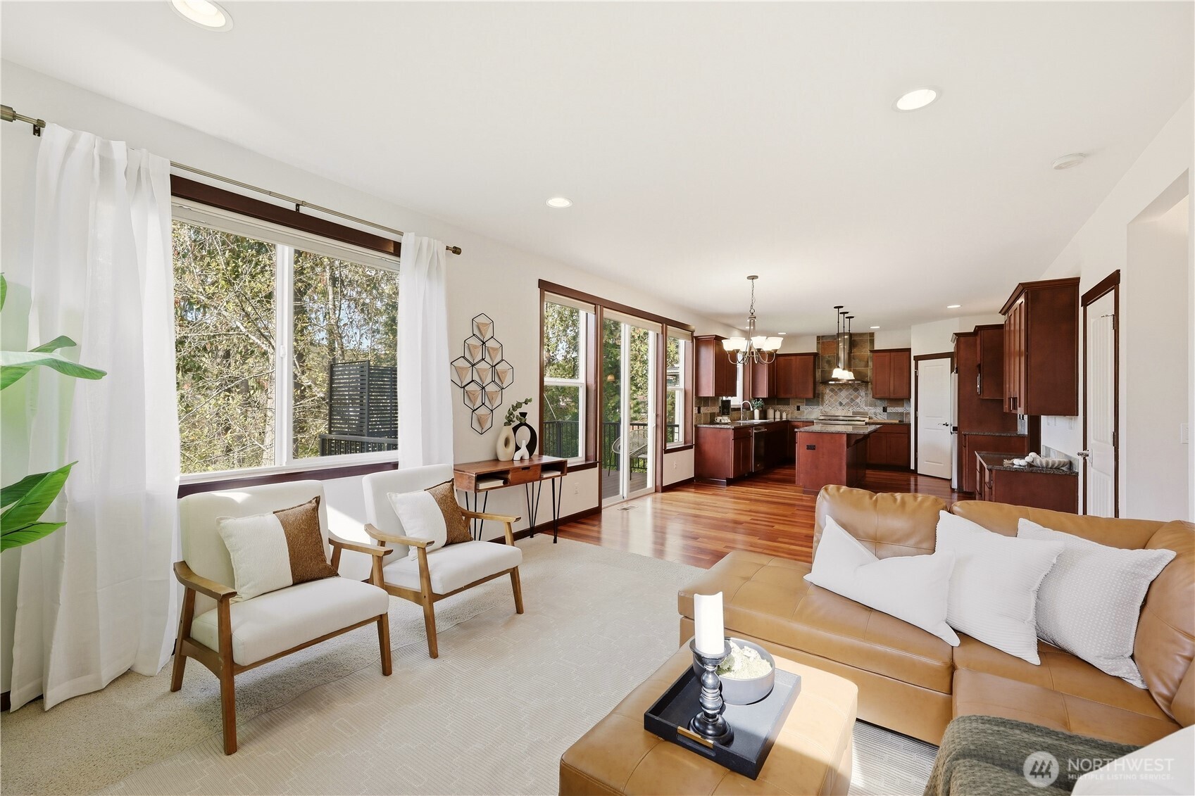 Open-plan living room and kitchen with a tan leather sectional, white chairs, and large windows.