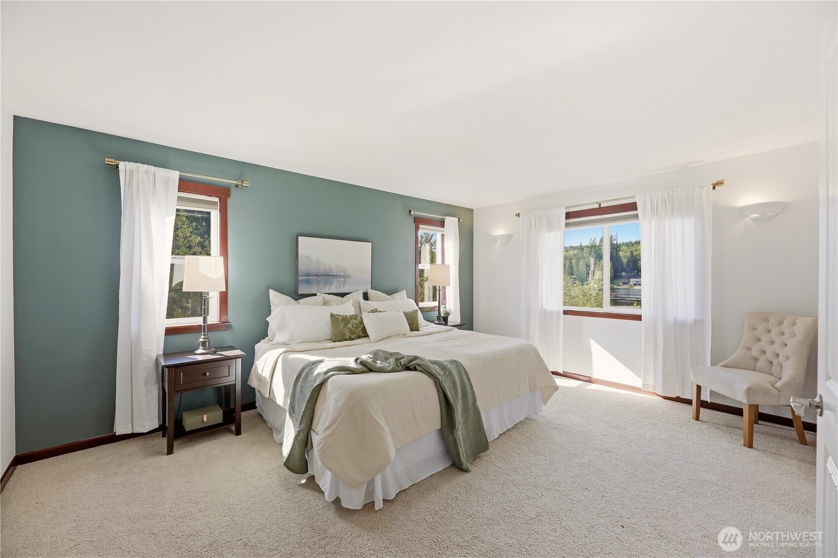 Furnished bedroom with a king-size bed, teal accent wall, and windows overlooking water.