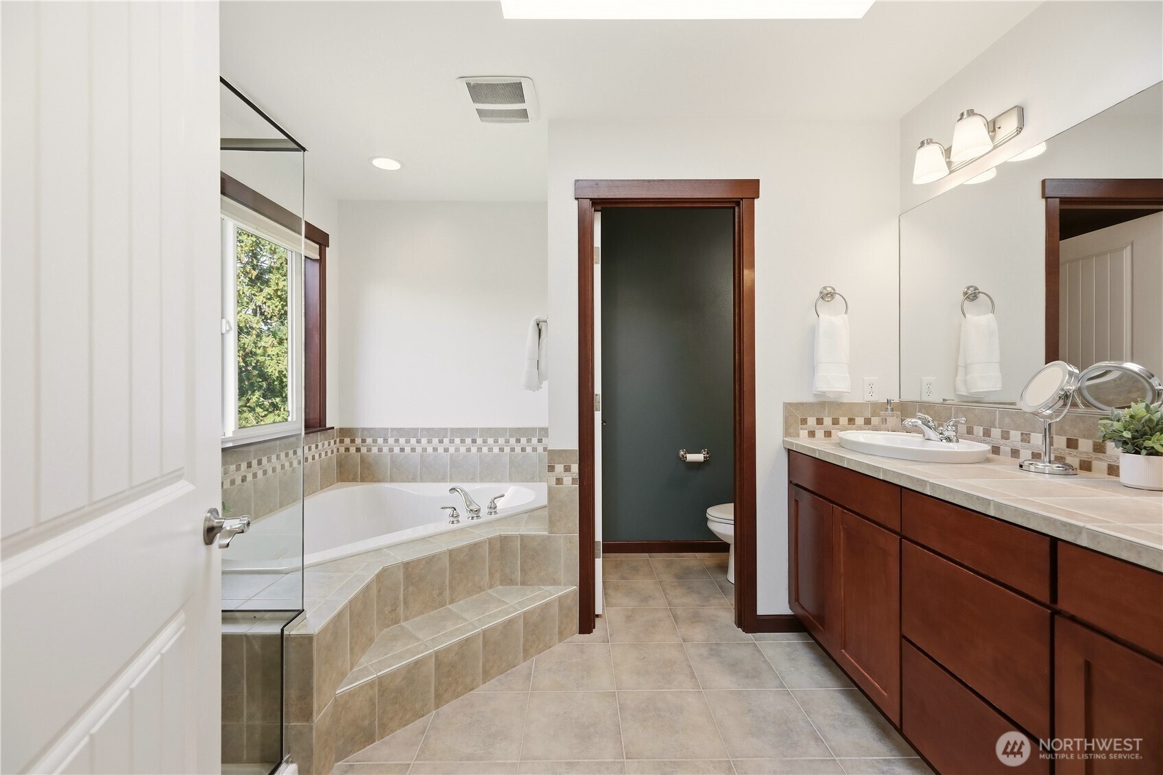 Bathroom with a tiled corner soaking tub, glass shower partition, and dark wood vanity.