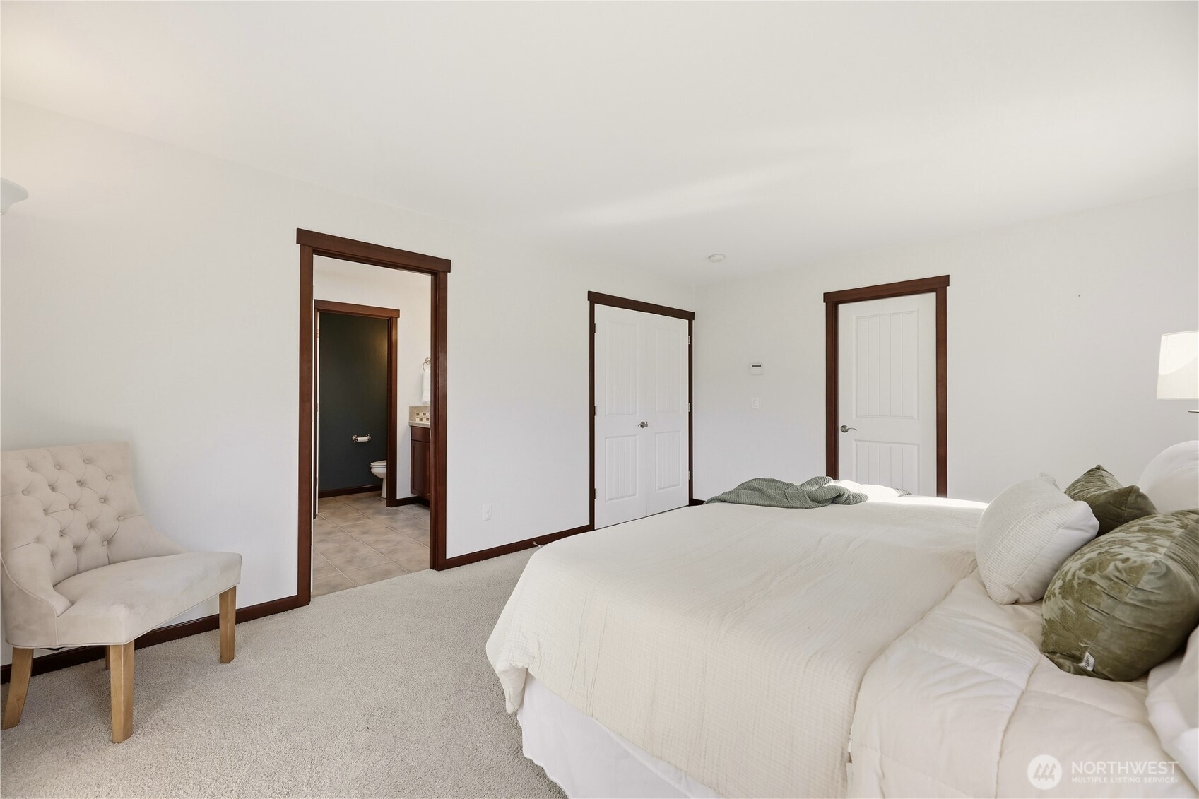 Bedroom with a white bed, tufted chair, and open doorway to an attached bathroom.
