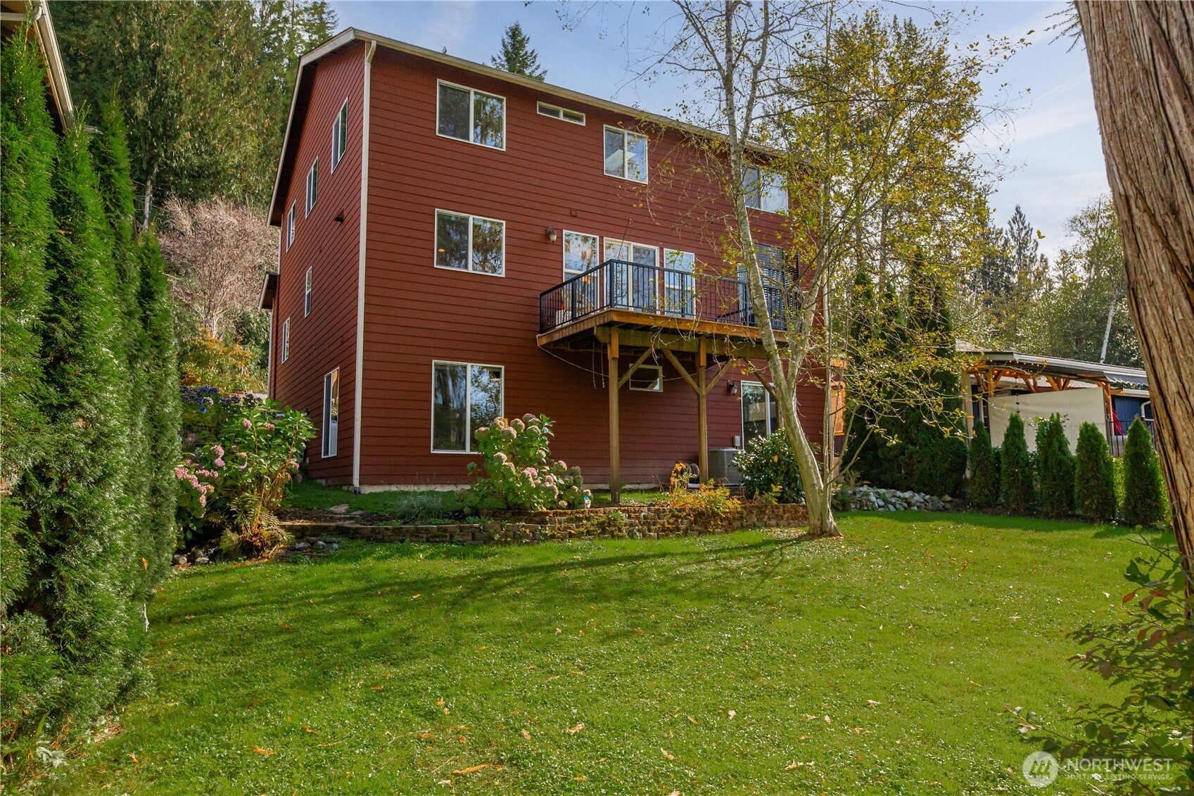 Red three-story house with a raised deck, surrounded by trees and a broad lawn.