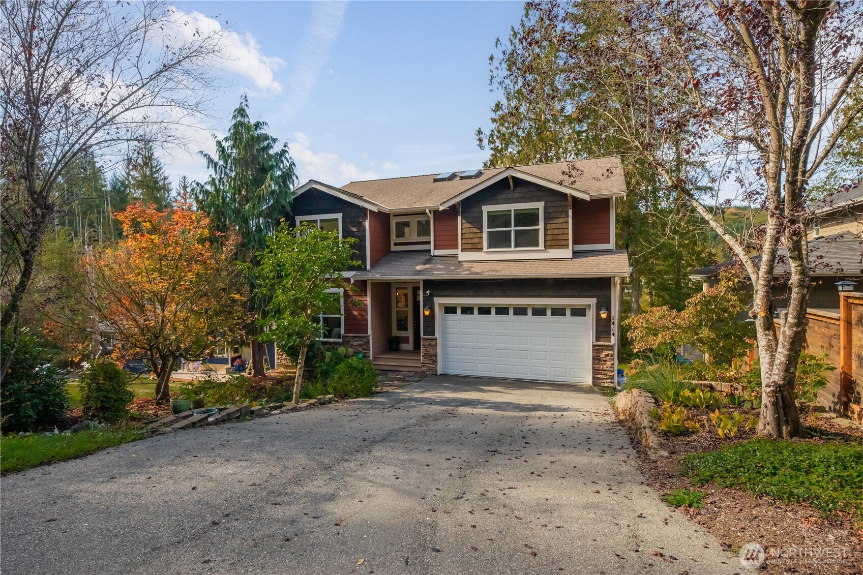 Two-story house with a white double garage door, broad driveway, and autumn trees.