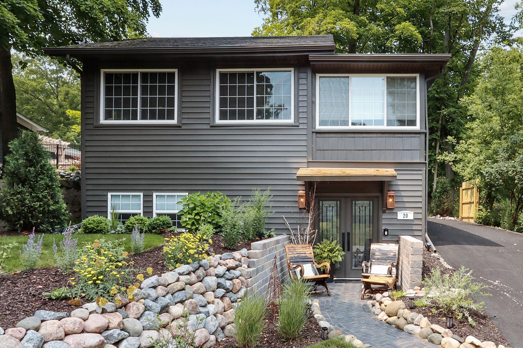 Gray-sided two-story home with a stone-edged garden path, landscaped flower beds, and a paved driveway.