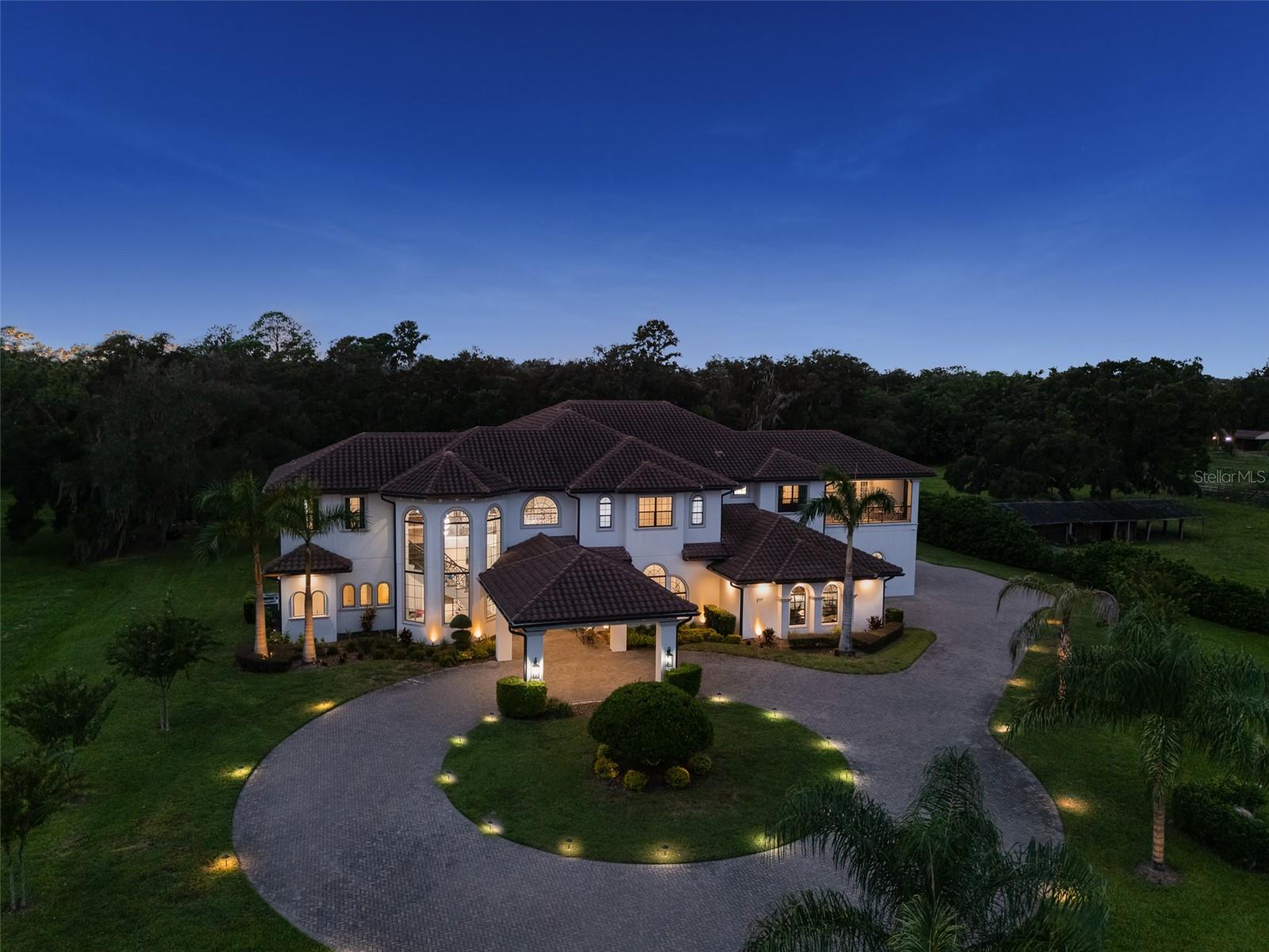 Two-story home with arched windows and a circular driveway, illuminated at dusk.
