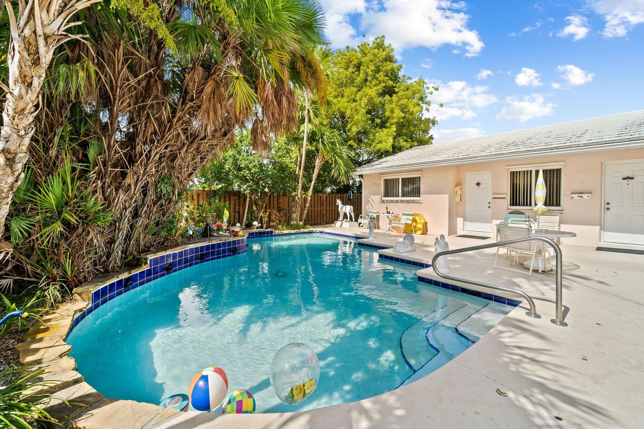 Curved backyard pool with blue tile edging, patio seating, and tropical palms.