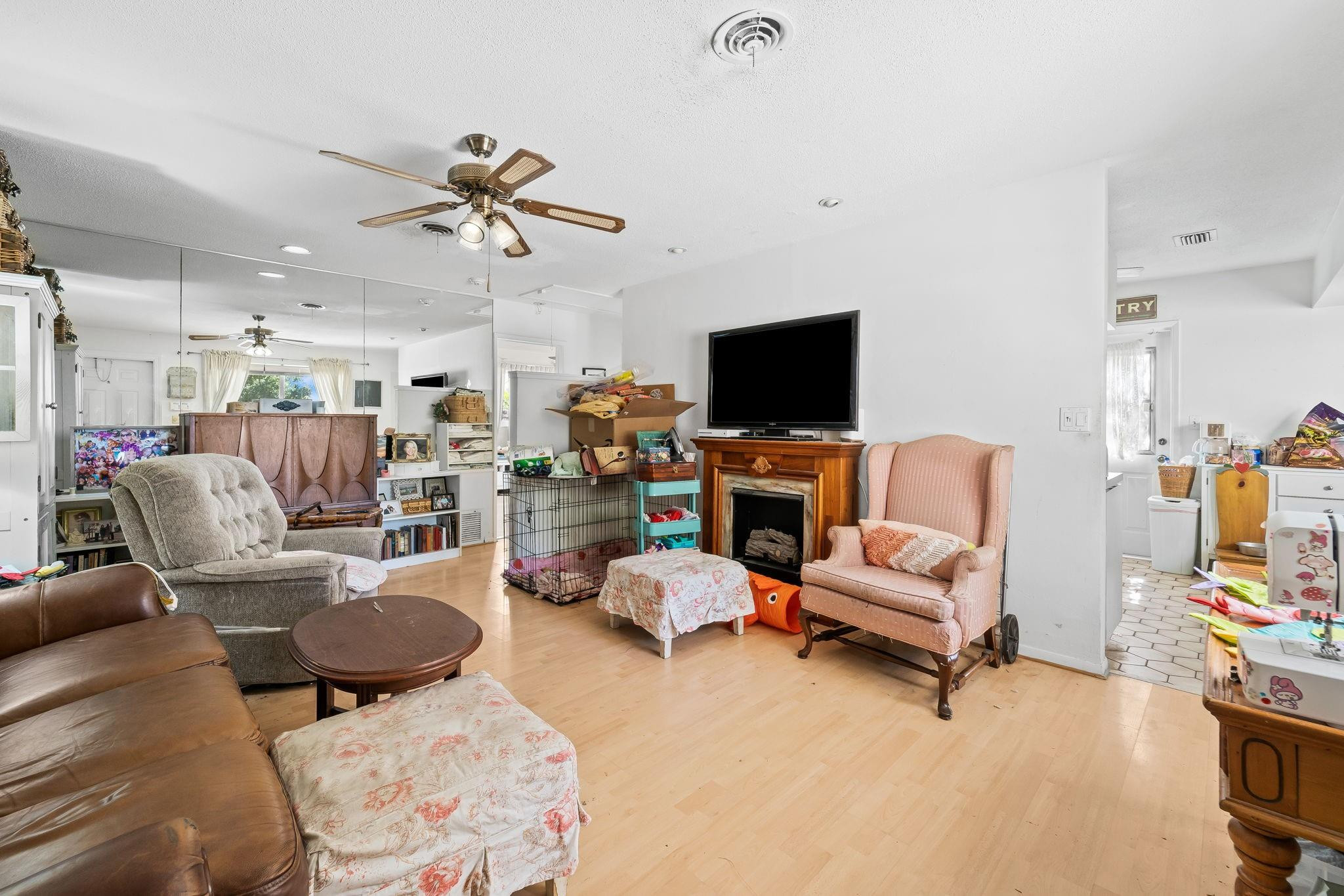 Living room with mirrored wall, ceiling fan, and television above a wooden fireplace.