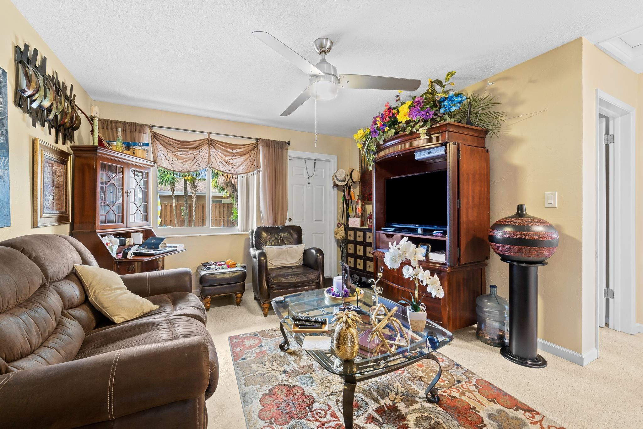 Furnished living room with brown leather seating, a glass coffee table, and a large wooden entertainment center.