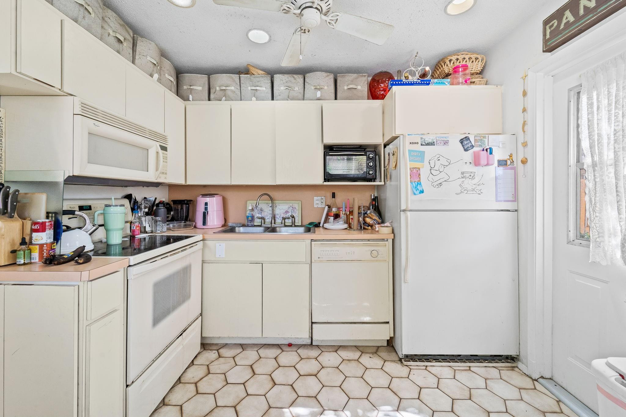 Kitchen with cream cabinets, a crowded countertop, white appliances, and hexagonal tile flooring.