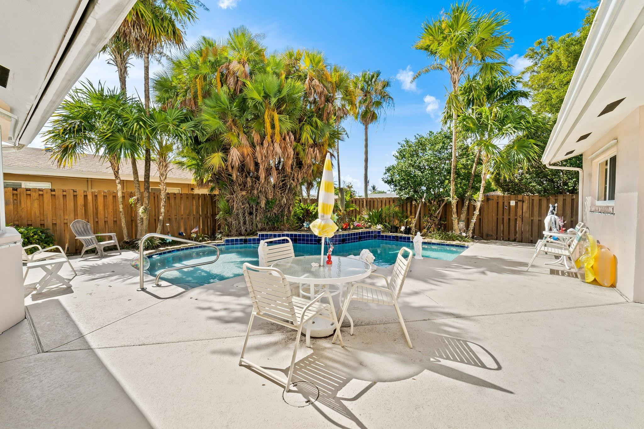 Backyard pool with a curved edge, palm trees, and white patio seating.