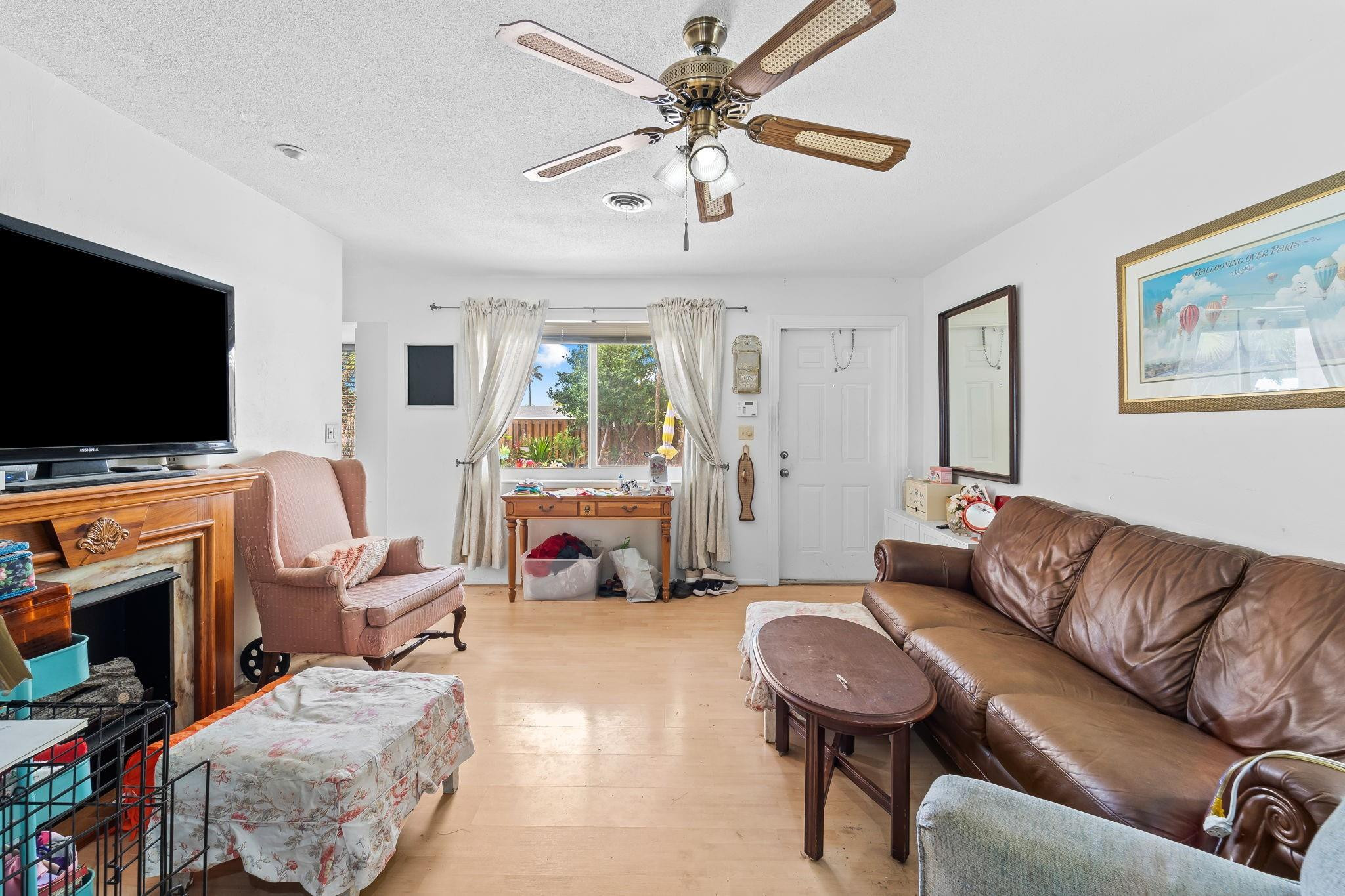 Living room with a brown leather sofa, pink armchair, and window overlooking a garden.