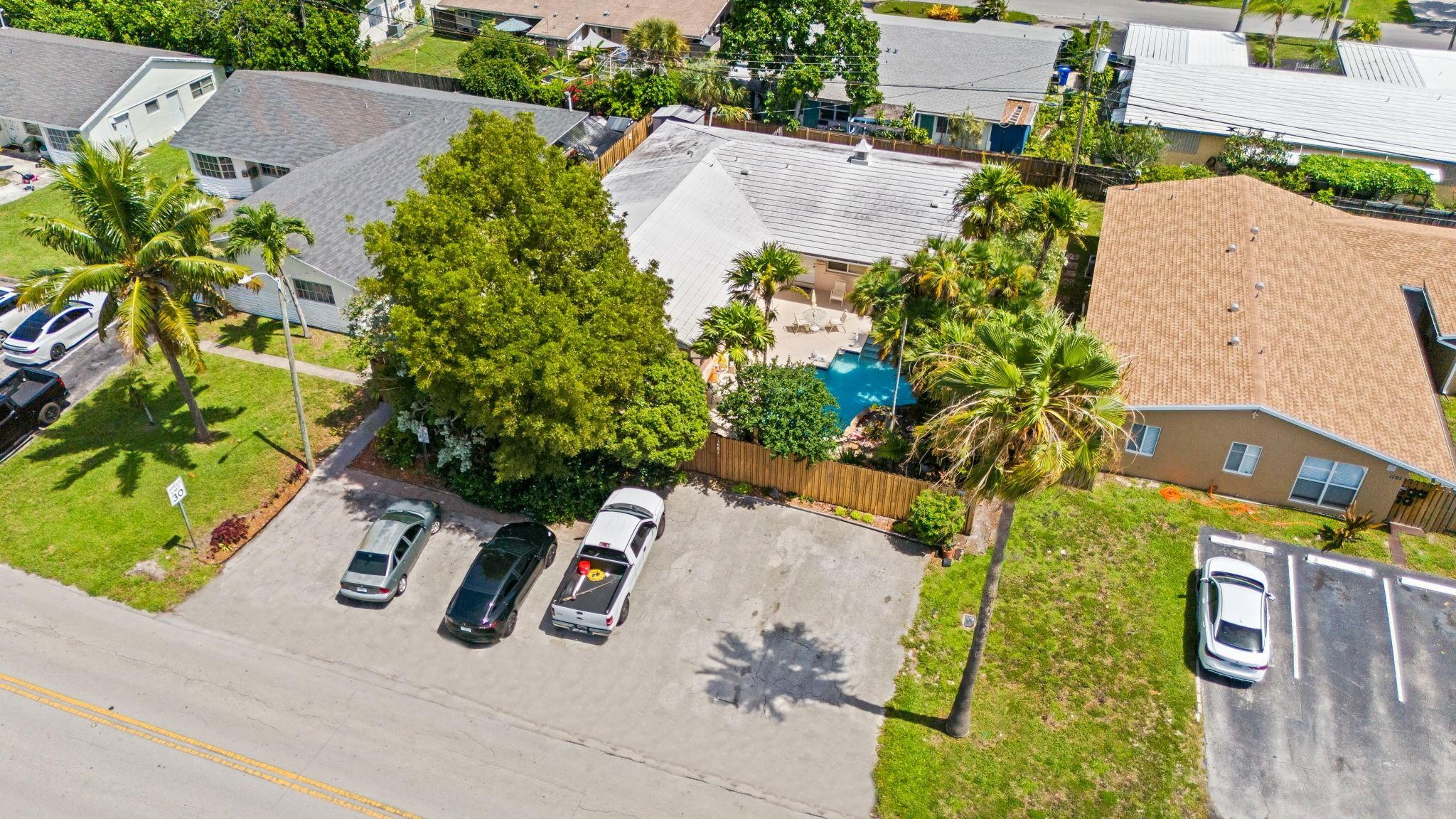 Aerial view of a house with a fenced backyard pool and patio among palm trees.