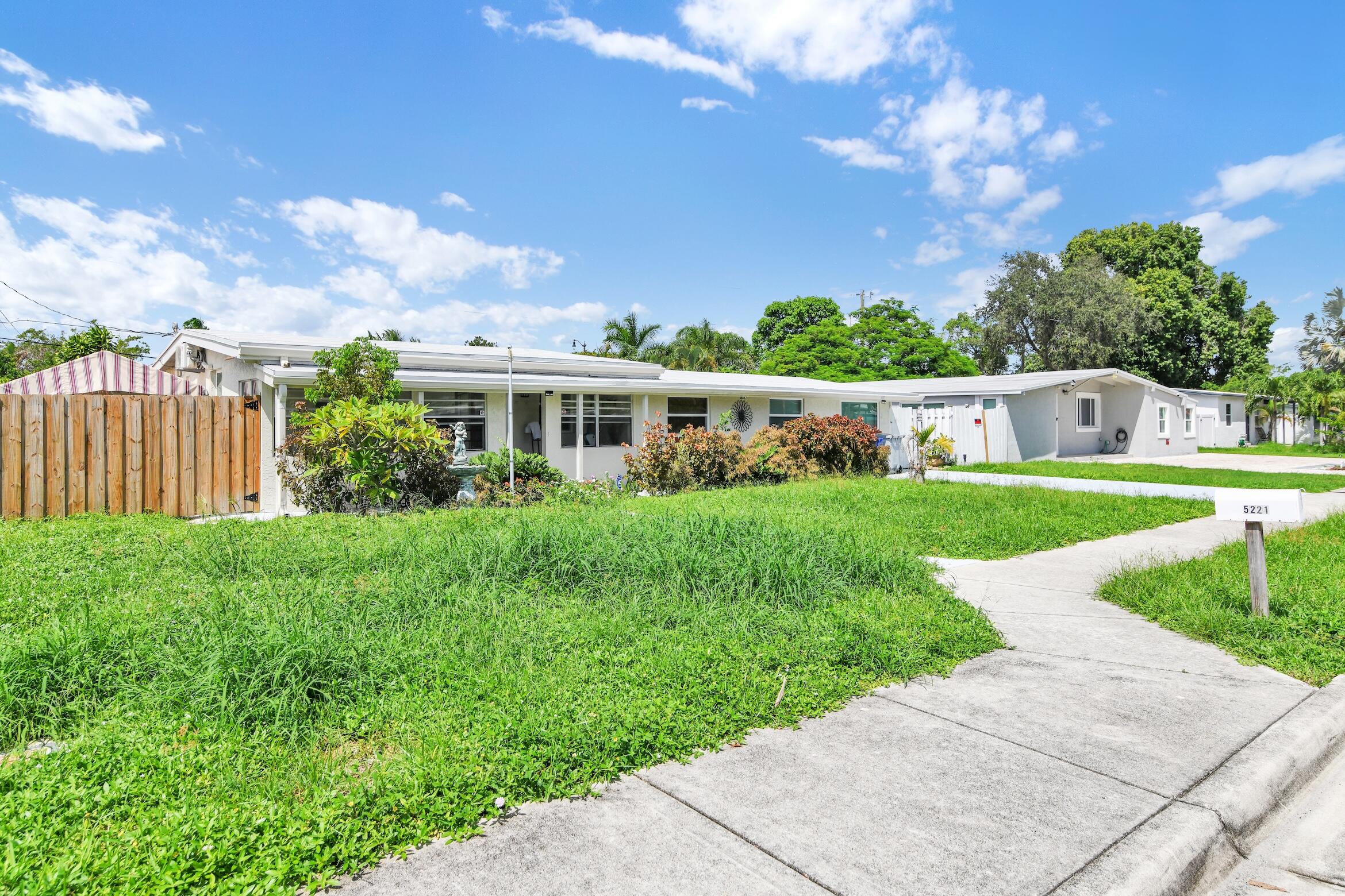 Single-story home with a broad lawn, landscaped shrubs, wooden fence, and mailbox marked 5221.