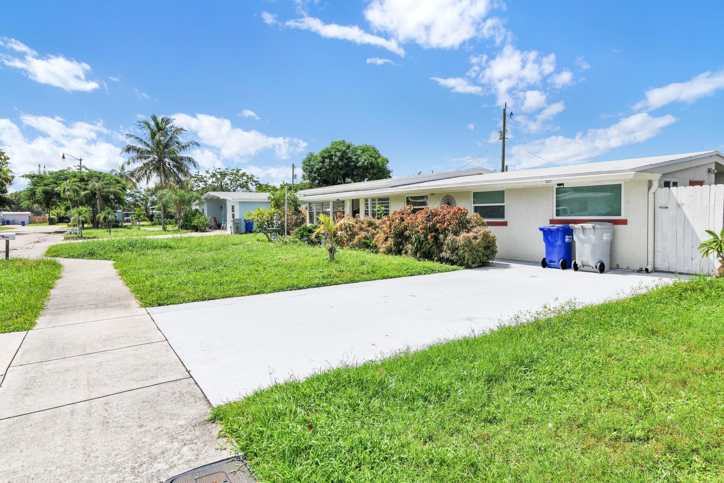 Single-story home with a broad driveway, green lawn, trimmed shrubs, and a palm tree.