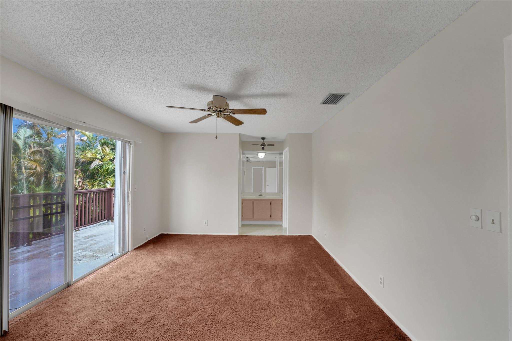 Empty carpeted bedroom with sliding glass doors to a balcony and a ceiling fan.