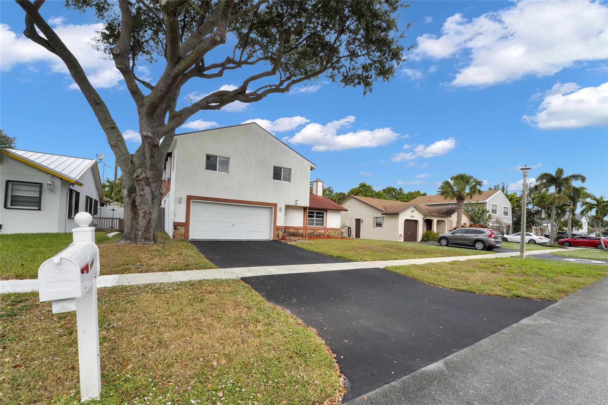 Two-story house with a double garage and dark driveway beneath a large oak tree.