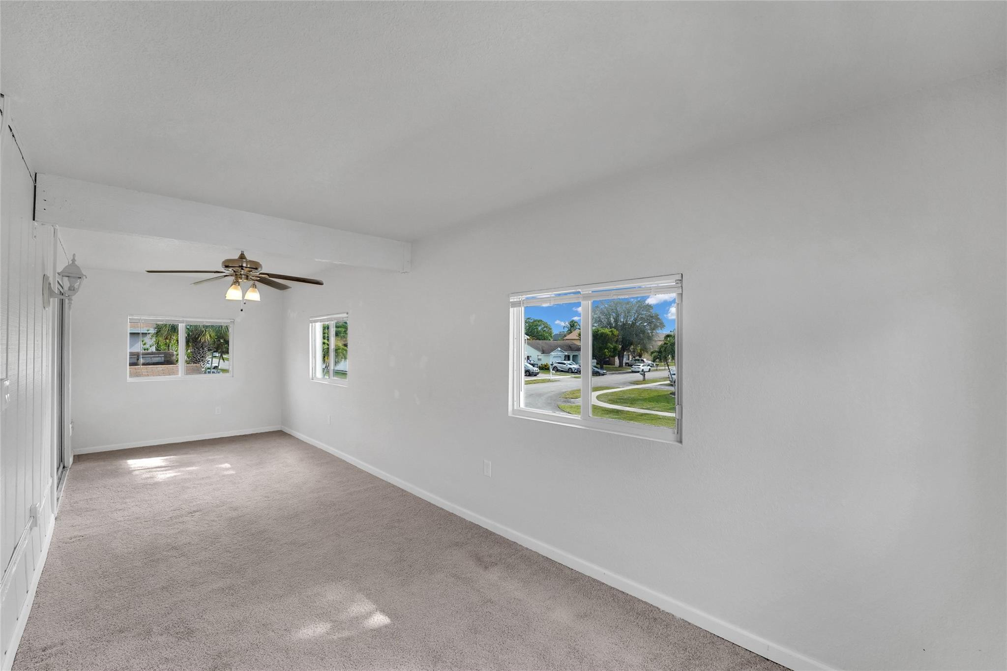 Empty living room with carpet, ceiling fan, and windows overlooking the street.