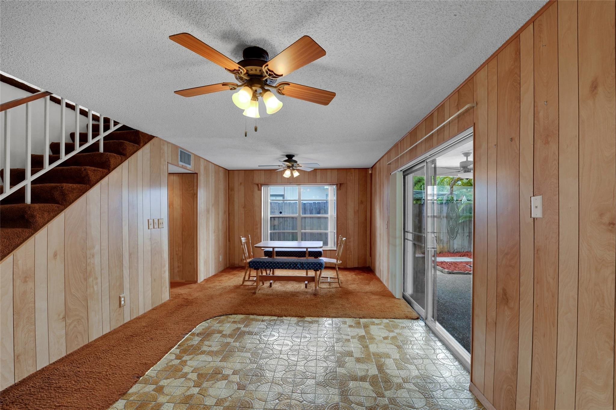 Wood-paneled dining area with staircase, brown carpet, patterned tile, and sliding glass doors.