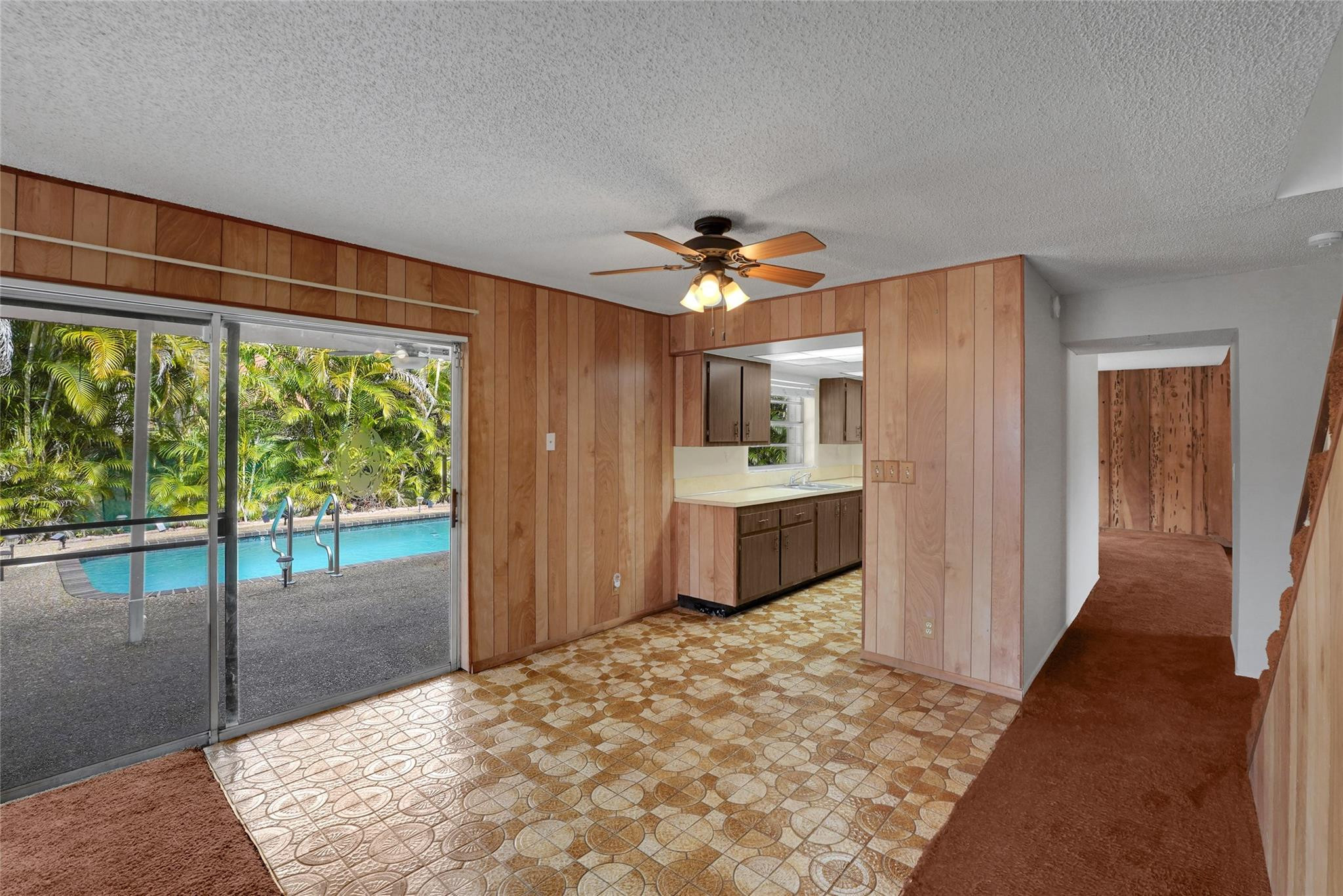 Unfurnished living area with wood paneling, patterned tile, a kitchen pass-through, and sliding doors overlooking a pool.