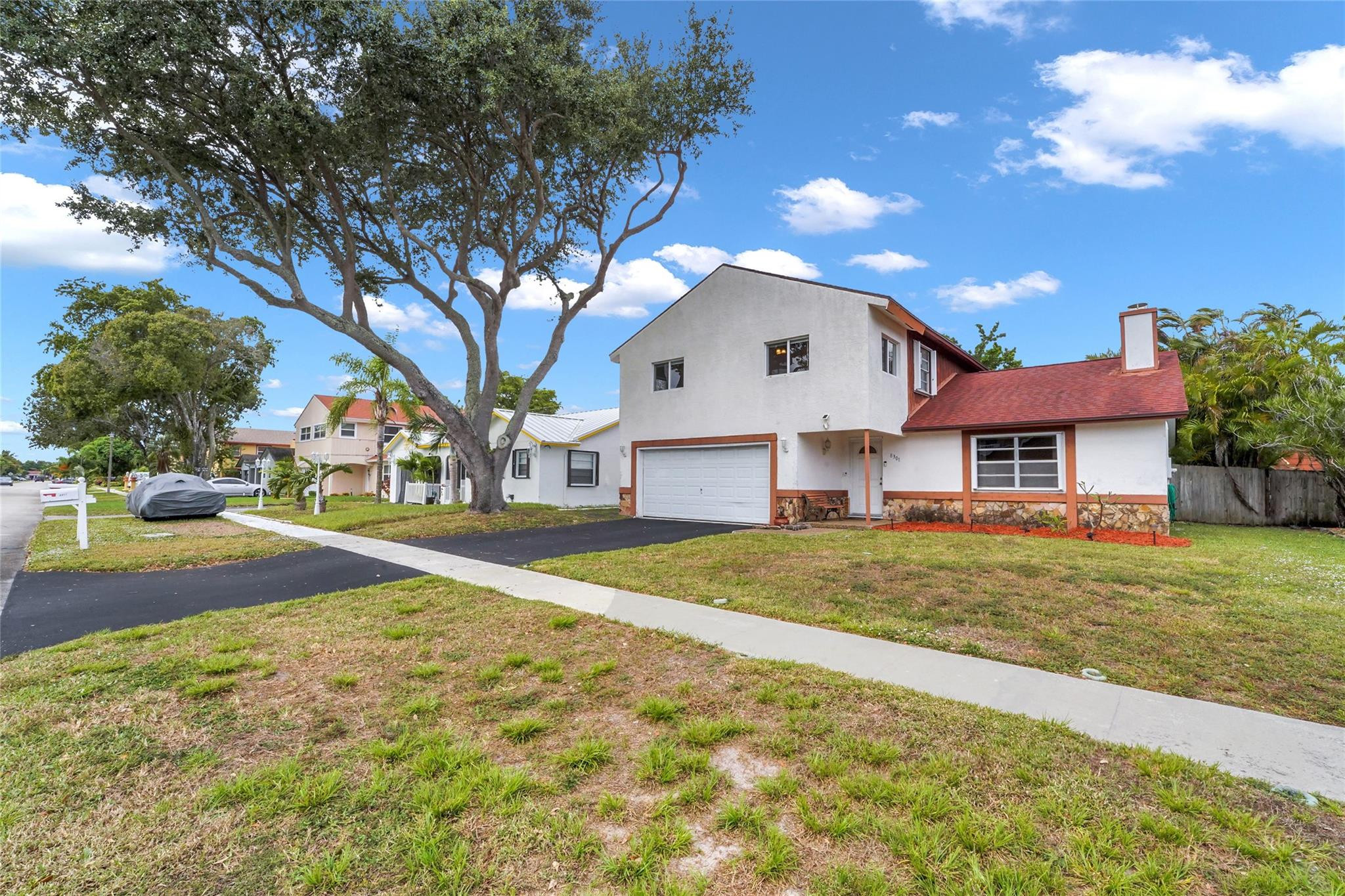 White two-story home with a red roof and garage beneath a large shade tree.