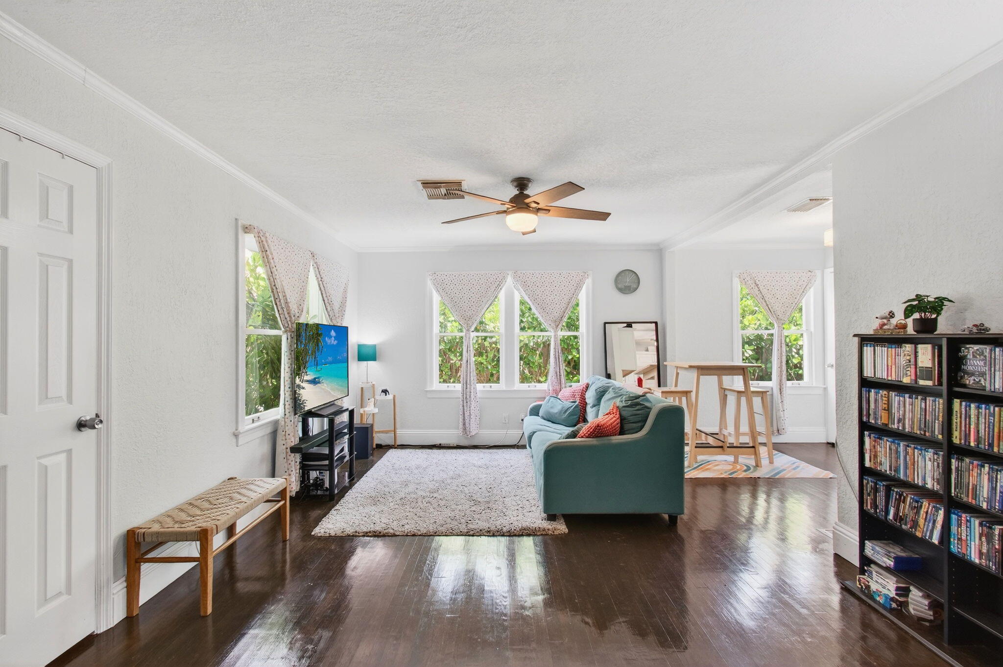 Bright living room with a teal sofa, dark hardwood floors, and curtained windows.