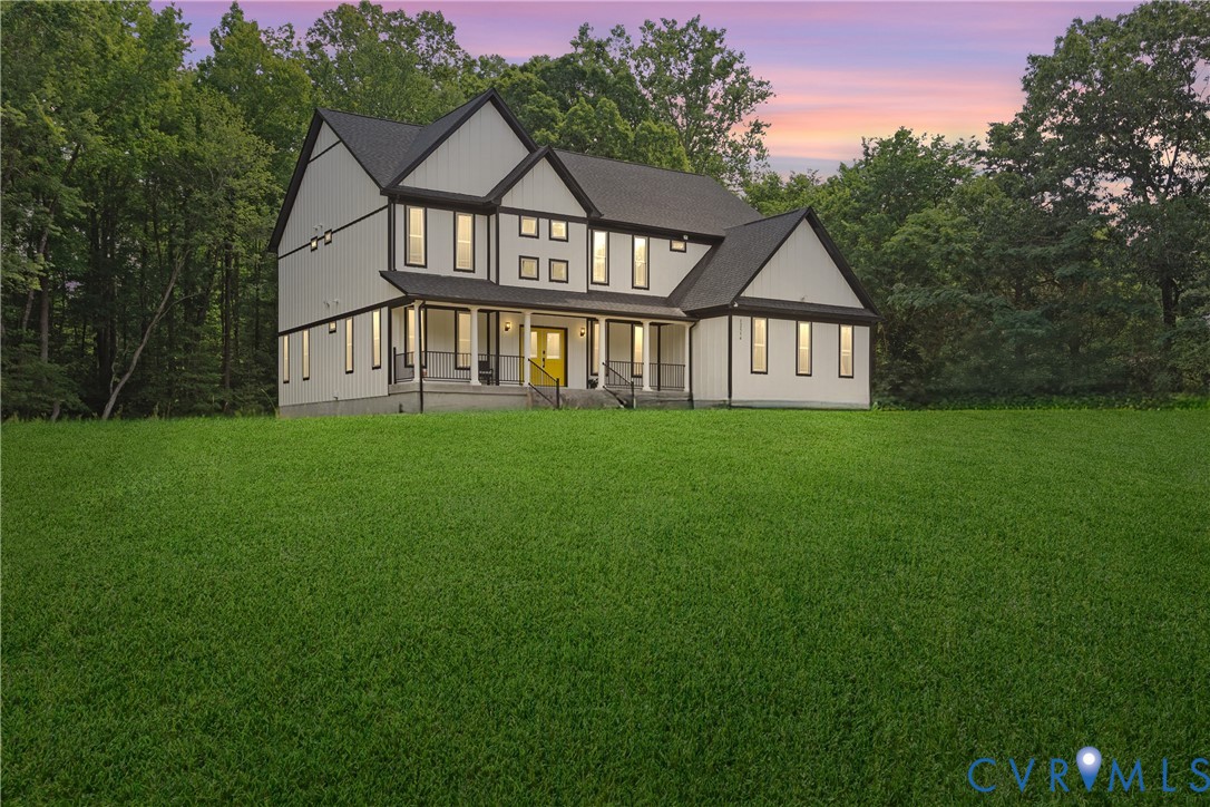 Two-story white house with dark gables, a lit front porch, and a broad lawn at dusk.