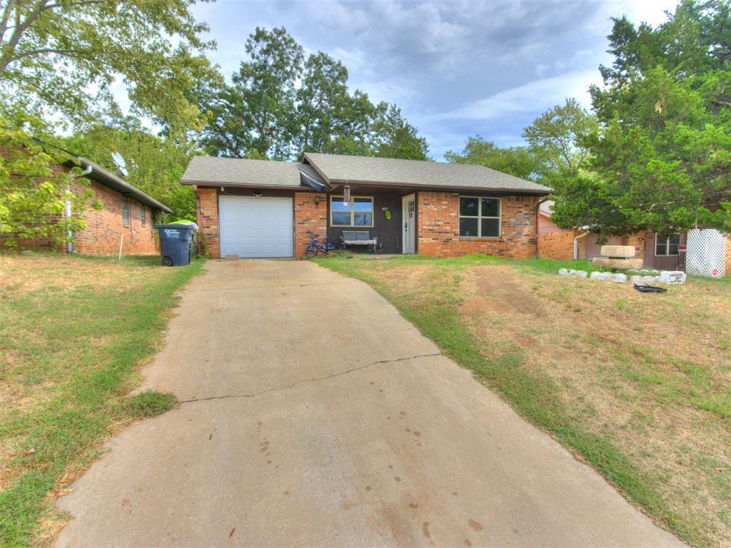 Single-story brick house with an attached garage, wide driveway, and mature trees.