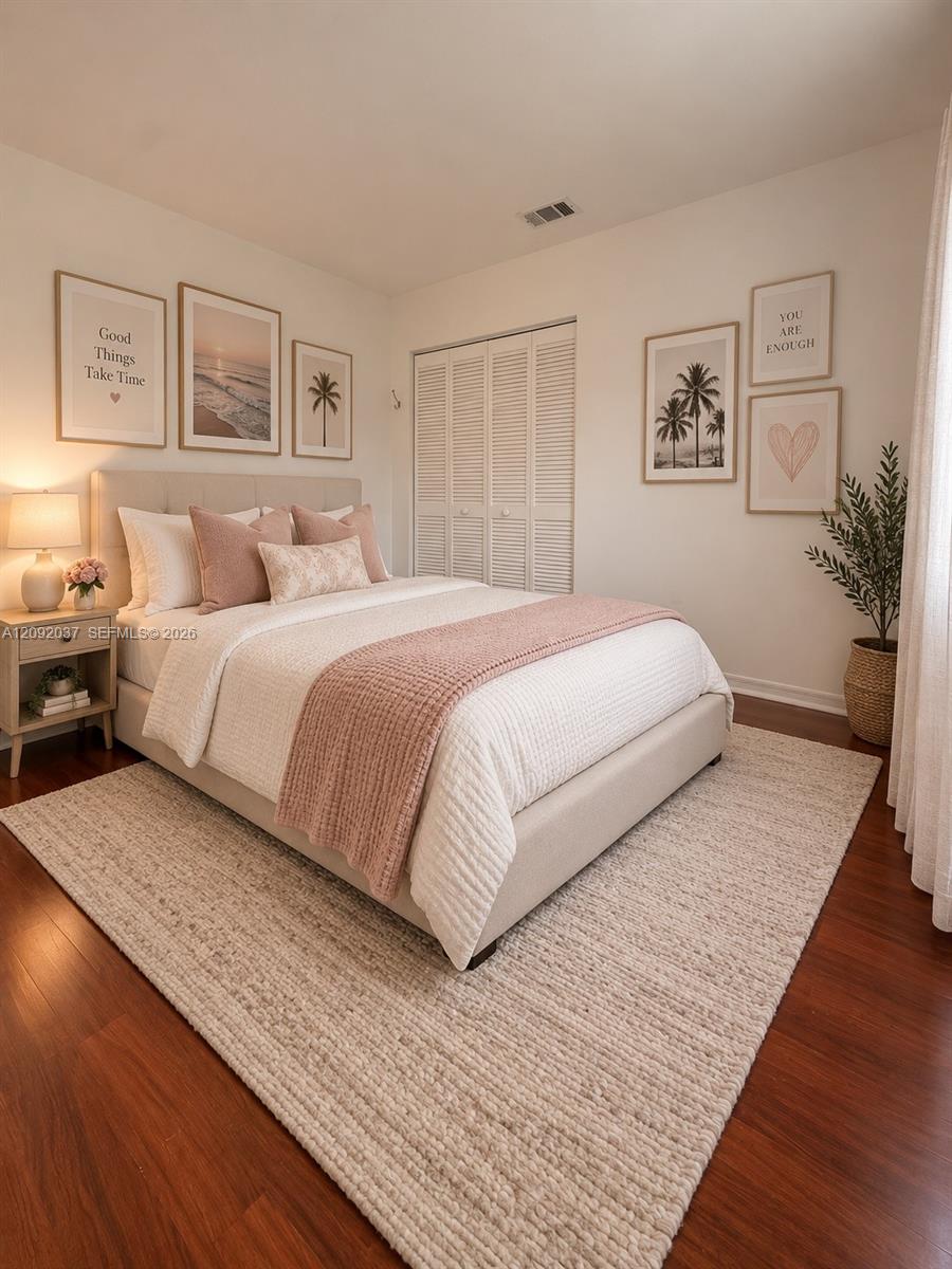 Furnished bedroom with a white bed, blush accents, palm prints, and white louvered closet doors.
