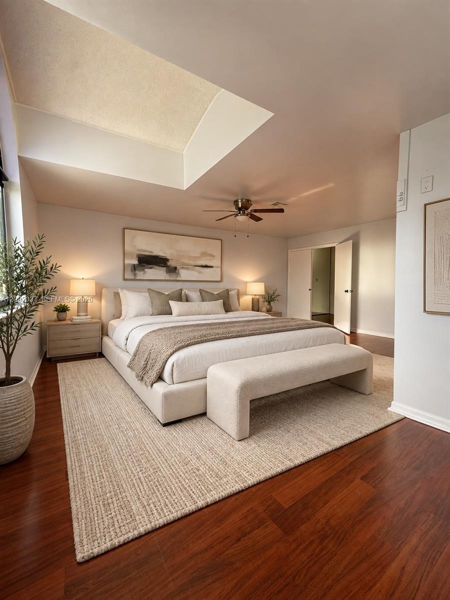 Staged bedroom with a large upholstered bed, woven rug, dark hardwood floors, and an angled vaulted ceiling.