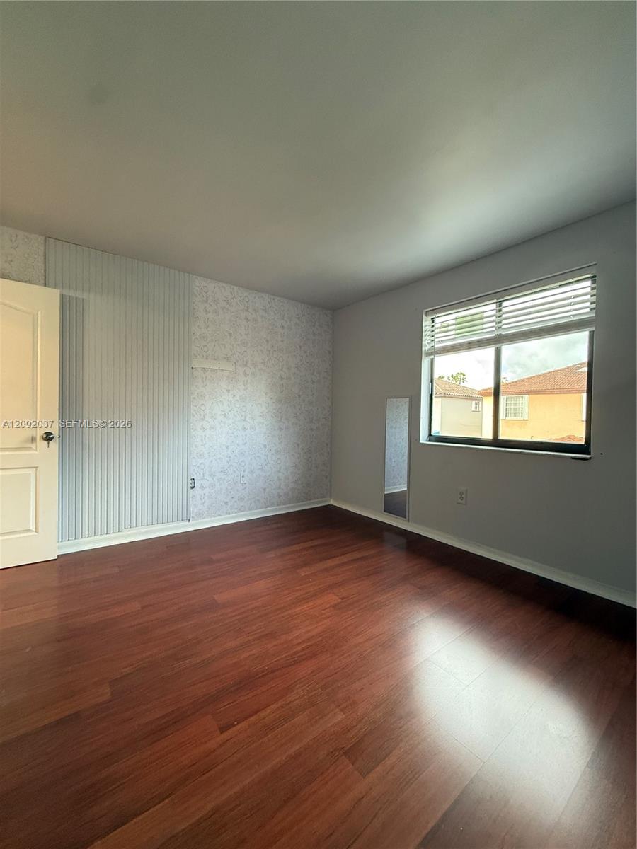 Unfurnished bedroom with reddish-brown flooring, patterned and striped wall finishes, and a window with blinds.
