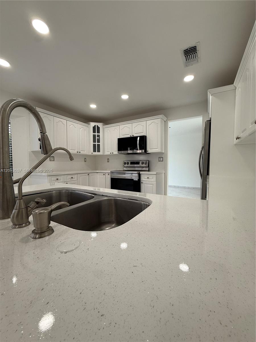 Kitchen with white cabinets, stainless steel appliances, and a large speckled countertop with a double sink.