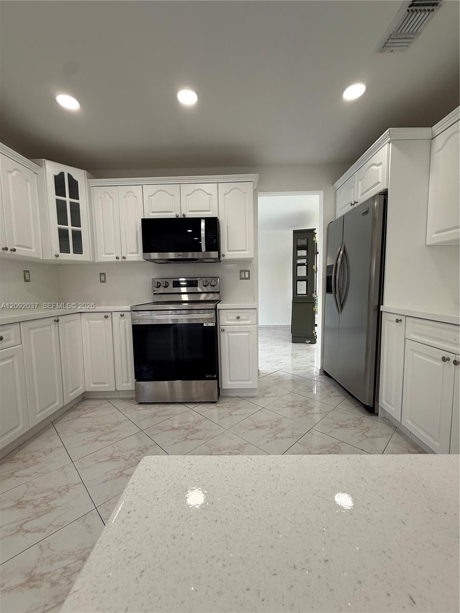 Kitchen with white cabinetry, stainless steel appliances, and a large speckled countertop.