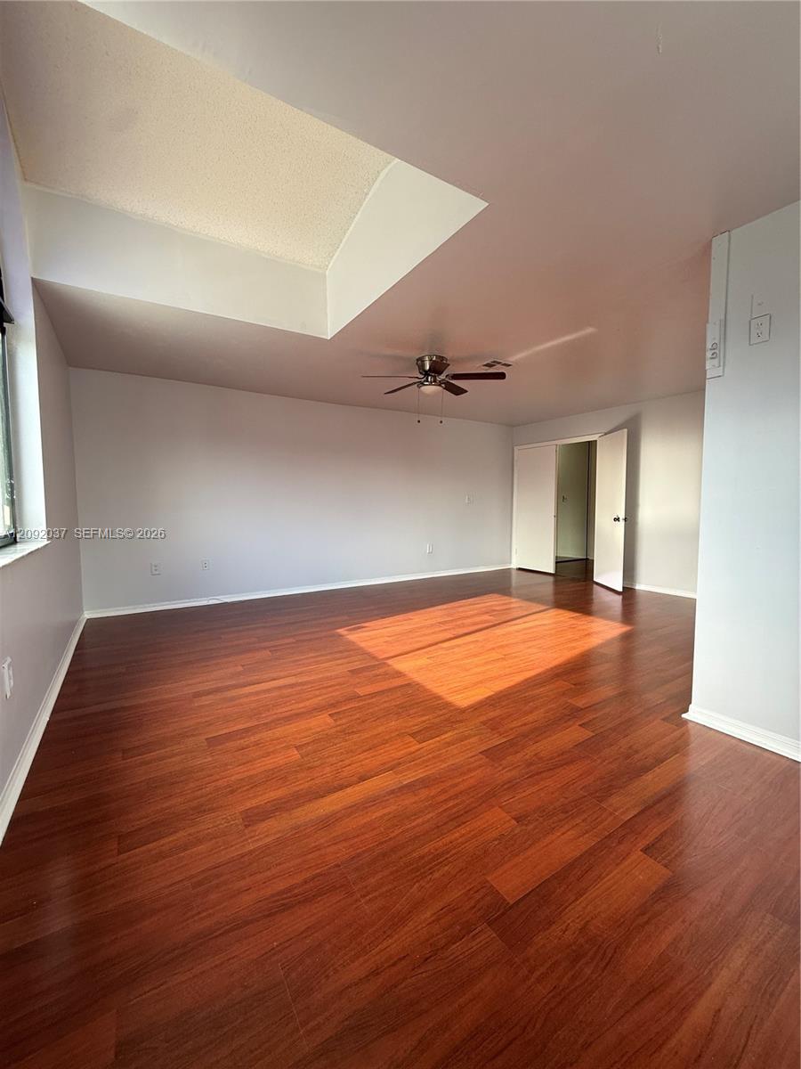 Empty room with reddish hardwood floors, a ceiling fan, and sunlight streaming through a window.