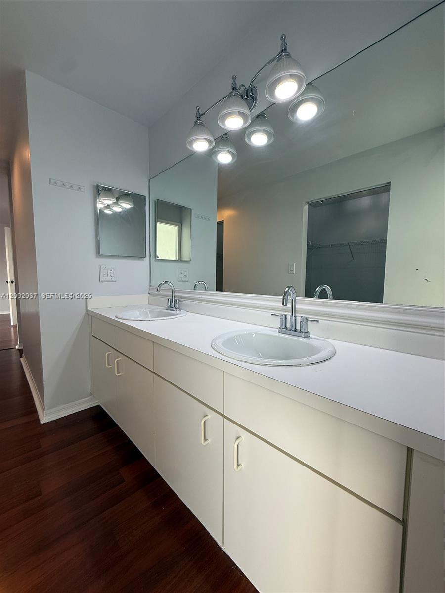 Bathroom double vanity with two sinks, a large mirror, chrome lights, and dark wood flooring.