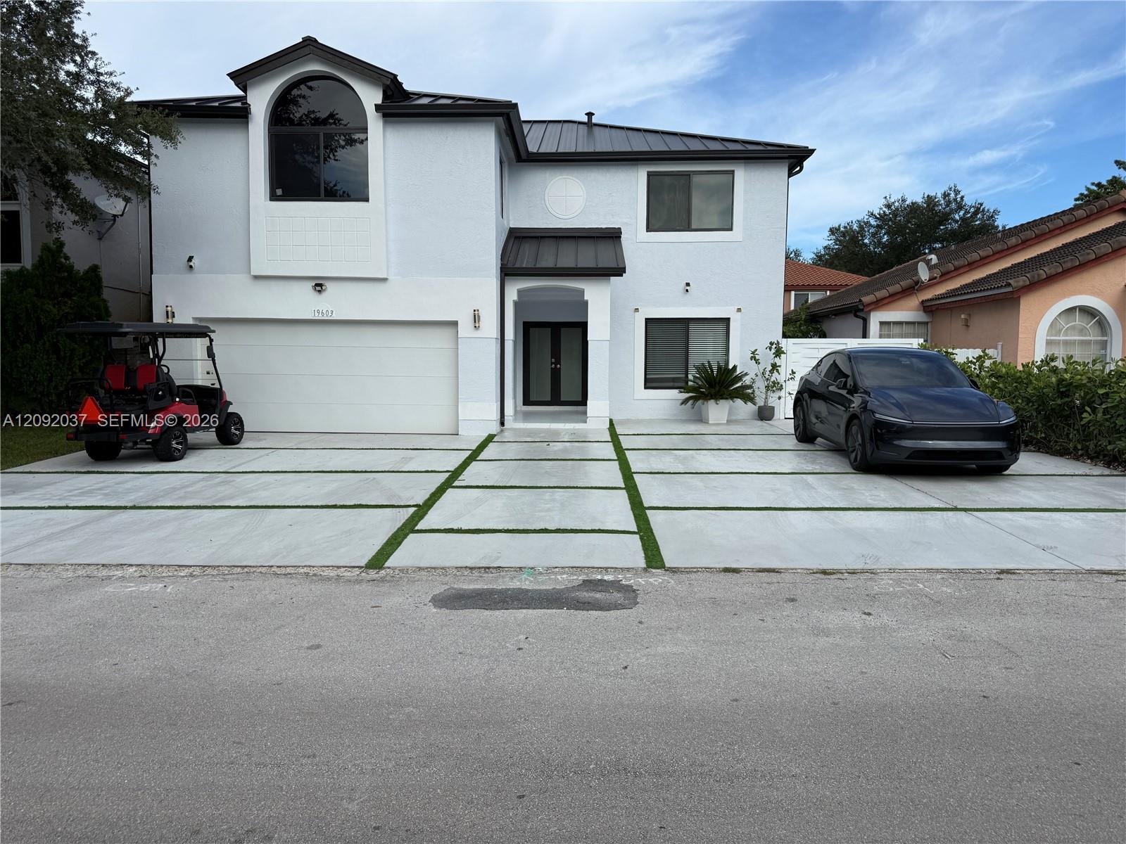 Two-story white stucco home with an arched upper window and grass-lined concrete driveway.