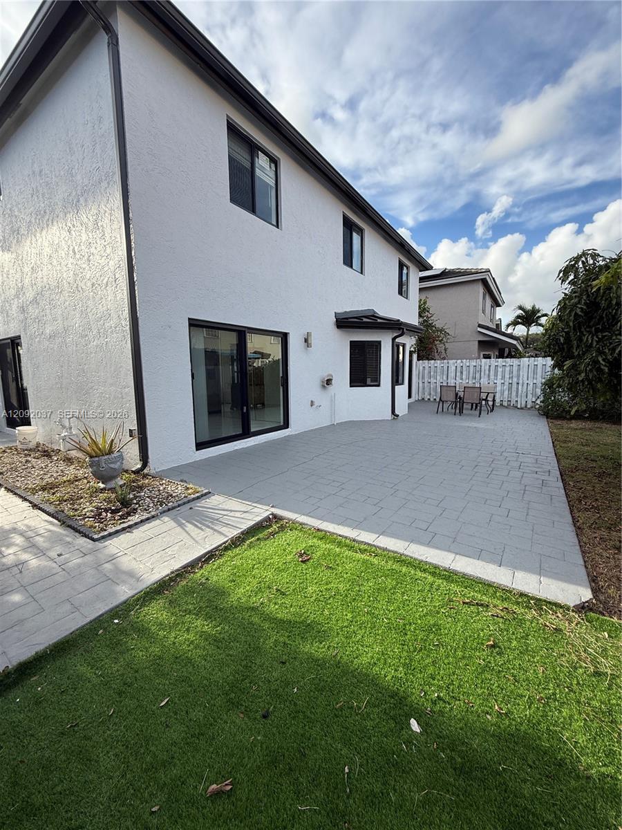 Two-story white stucco home with a broad paved backyard patio and outdoor dining set.