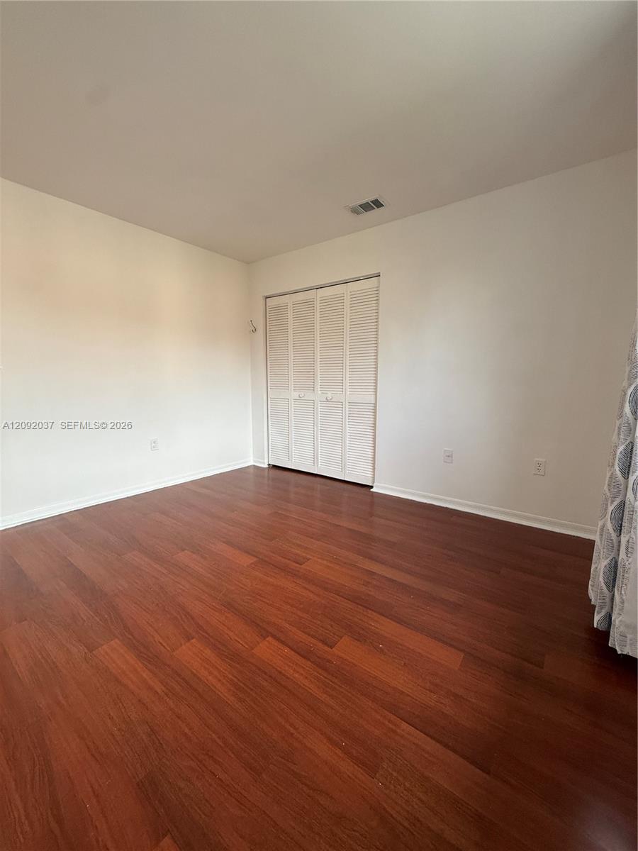 Vacant bedroom with reddish hardwood floors and white louvered closet doors.