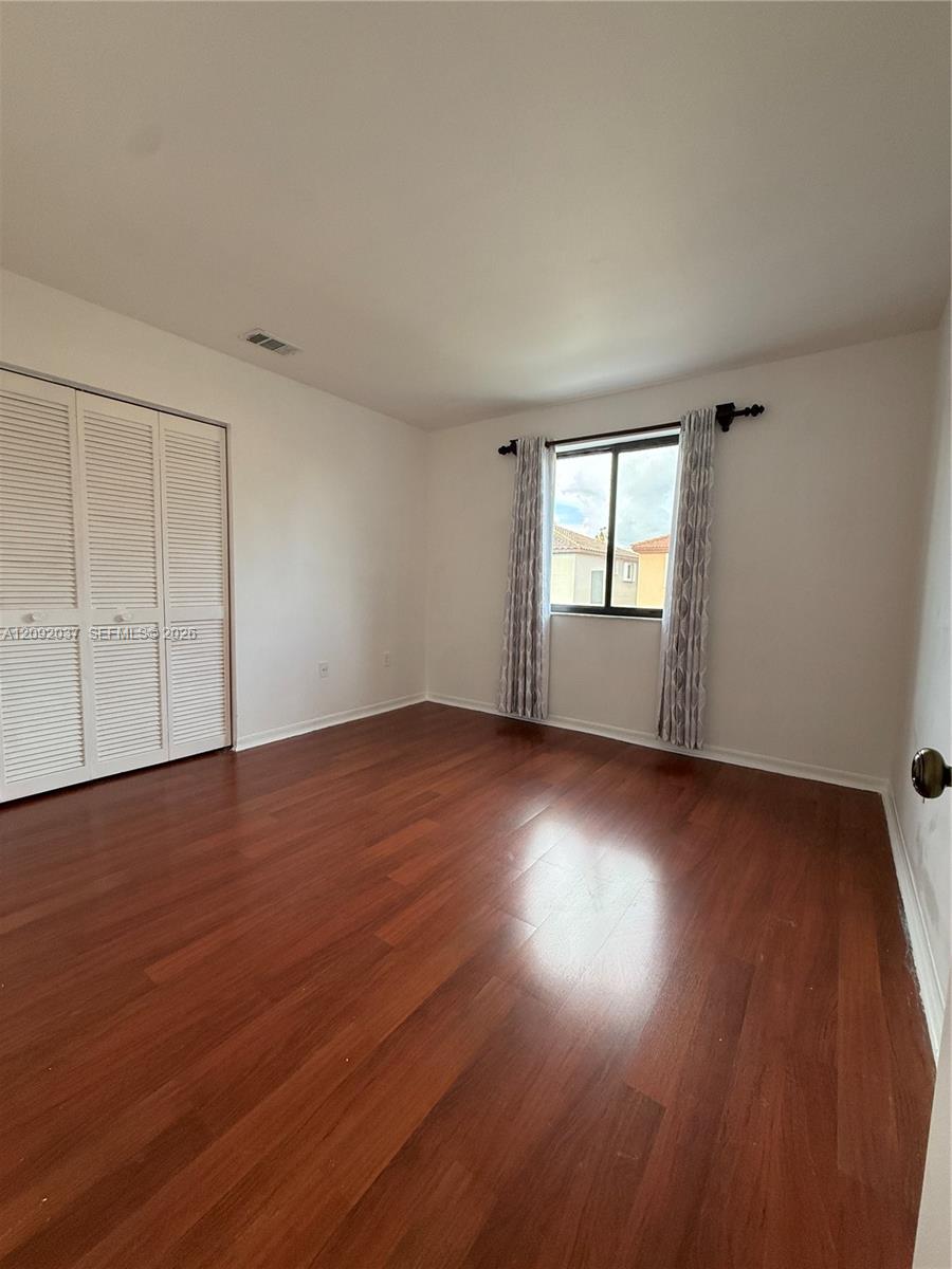 Empty bedroom with hardwood floors, louvered closet doors, and a curtained window.