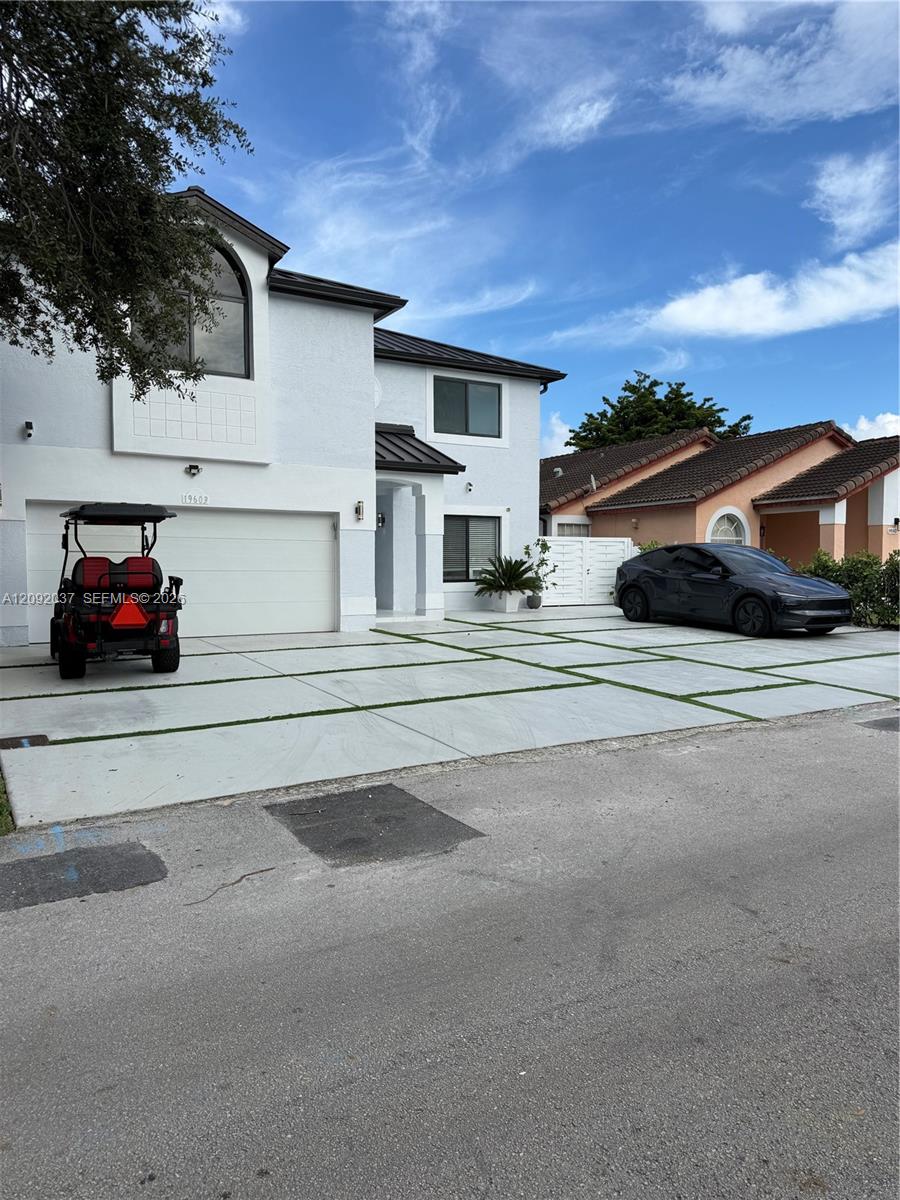 Two-story white stucco home with dark metal roof, arched window, and wide driveway.