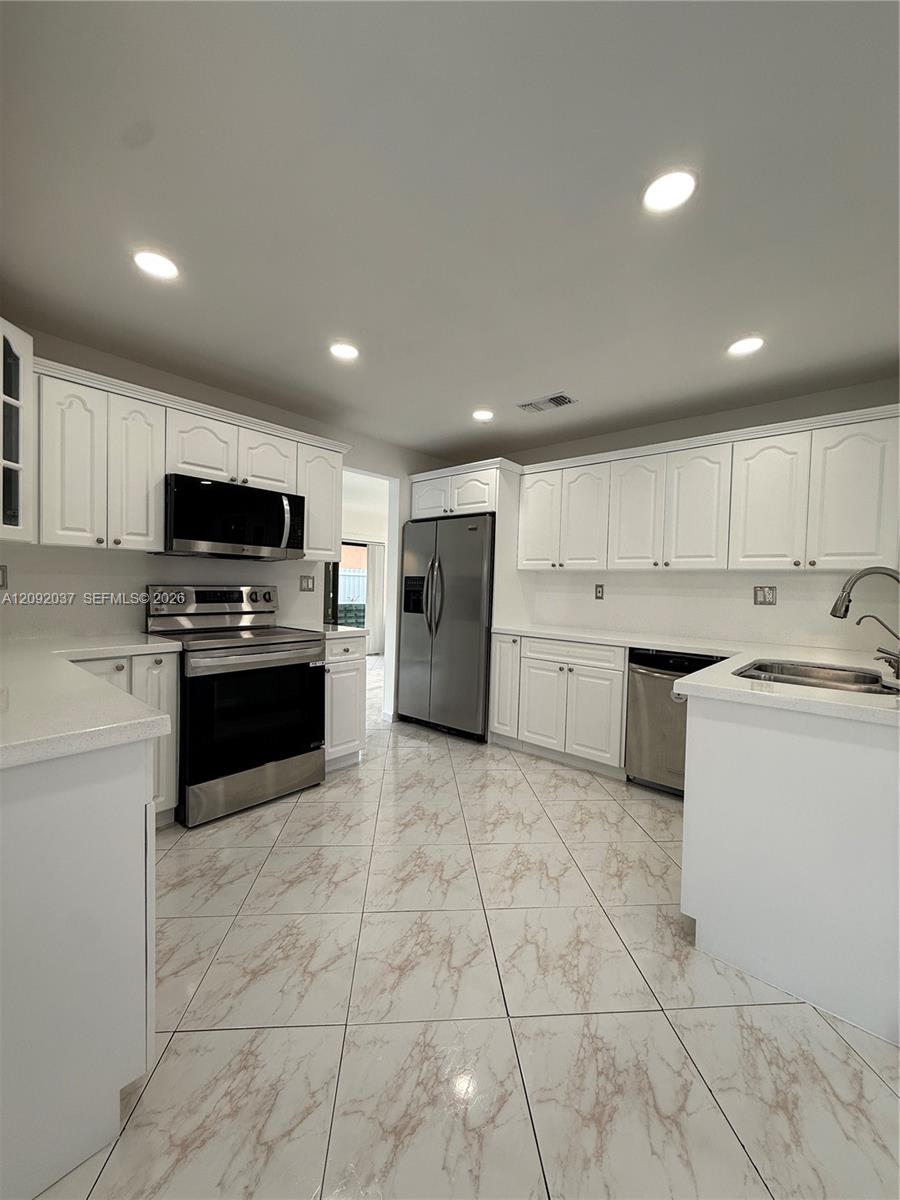 Kitchen with white cabinets, stainless steel appliances, and large marble-look tile flooring.
