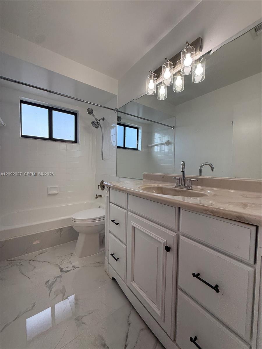 Bathroom with a mirrored vanity, white paneled cabinets, bathtub, and marble-patterned tile floor.