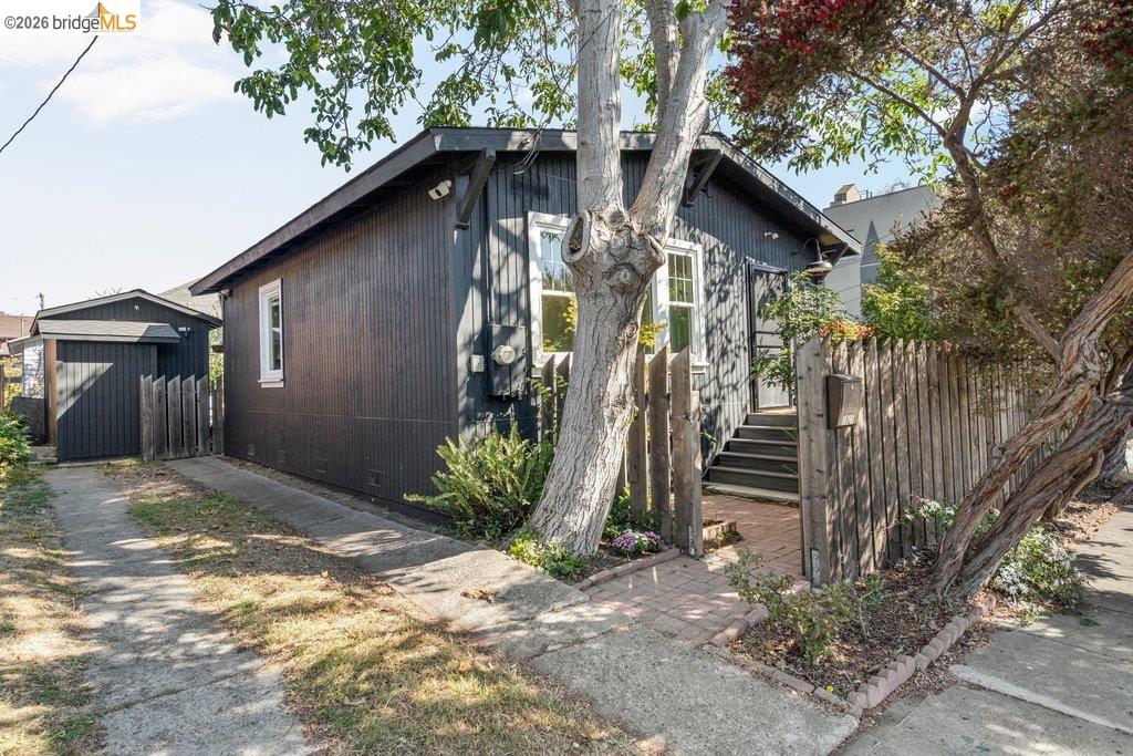 Dark charcoal house partly screened by a large tree, with a detached garage and fenced entry walkway.