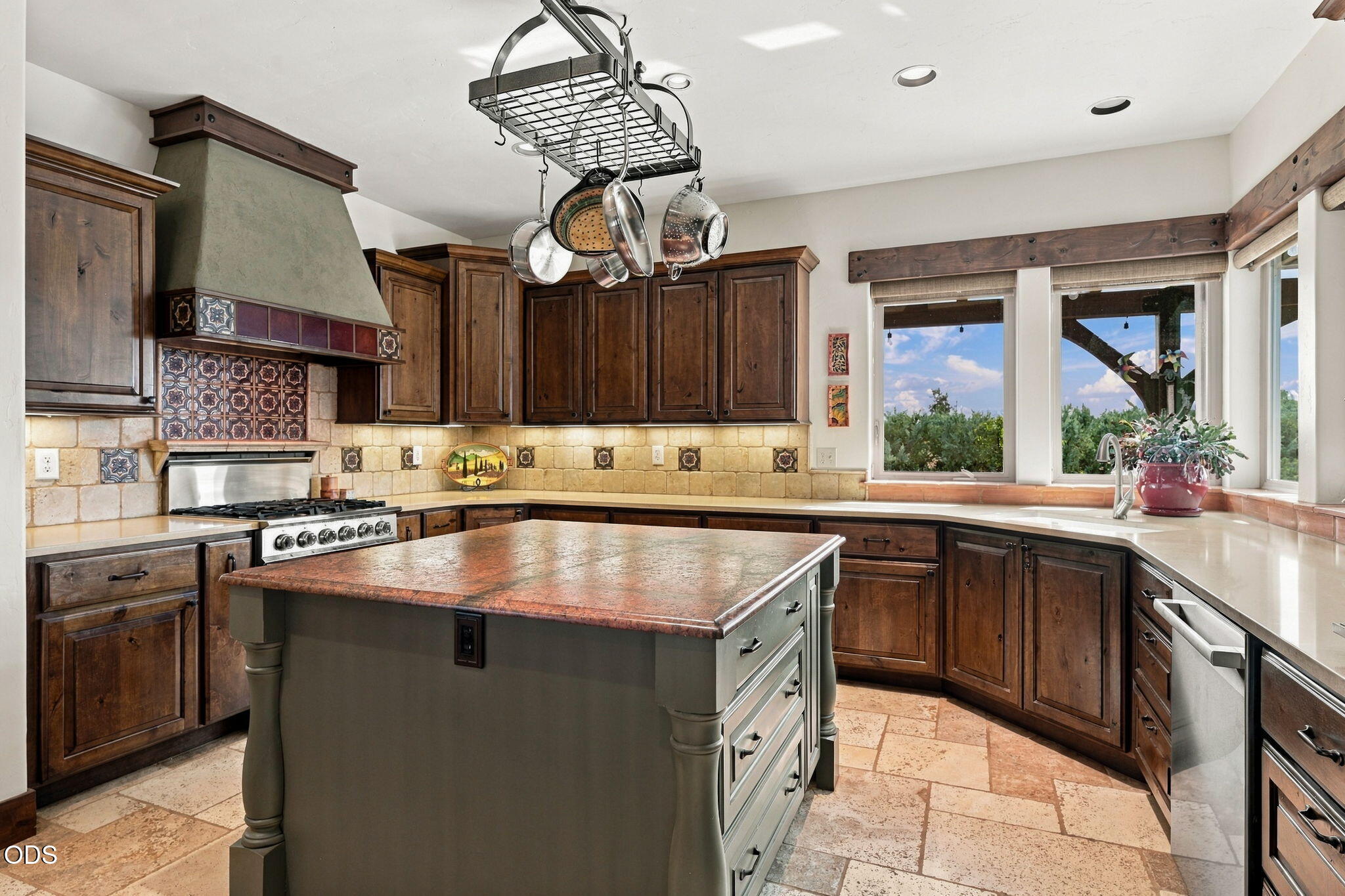 Kitchen with dark wood cabinetry, a large stone-topped island, tiled range hood, and bright windows over the sink.