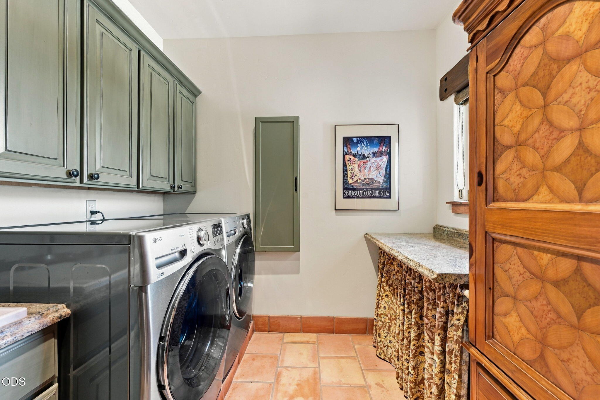 Laundry room with front-loading washer and dryer, sage-green cabinets, and a carved wooden cabinet.