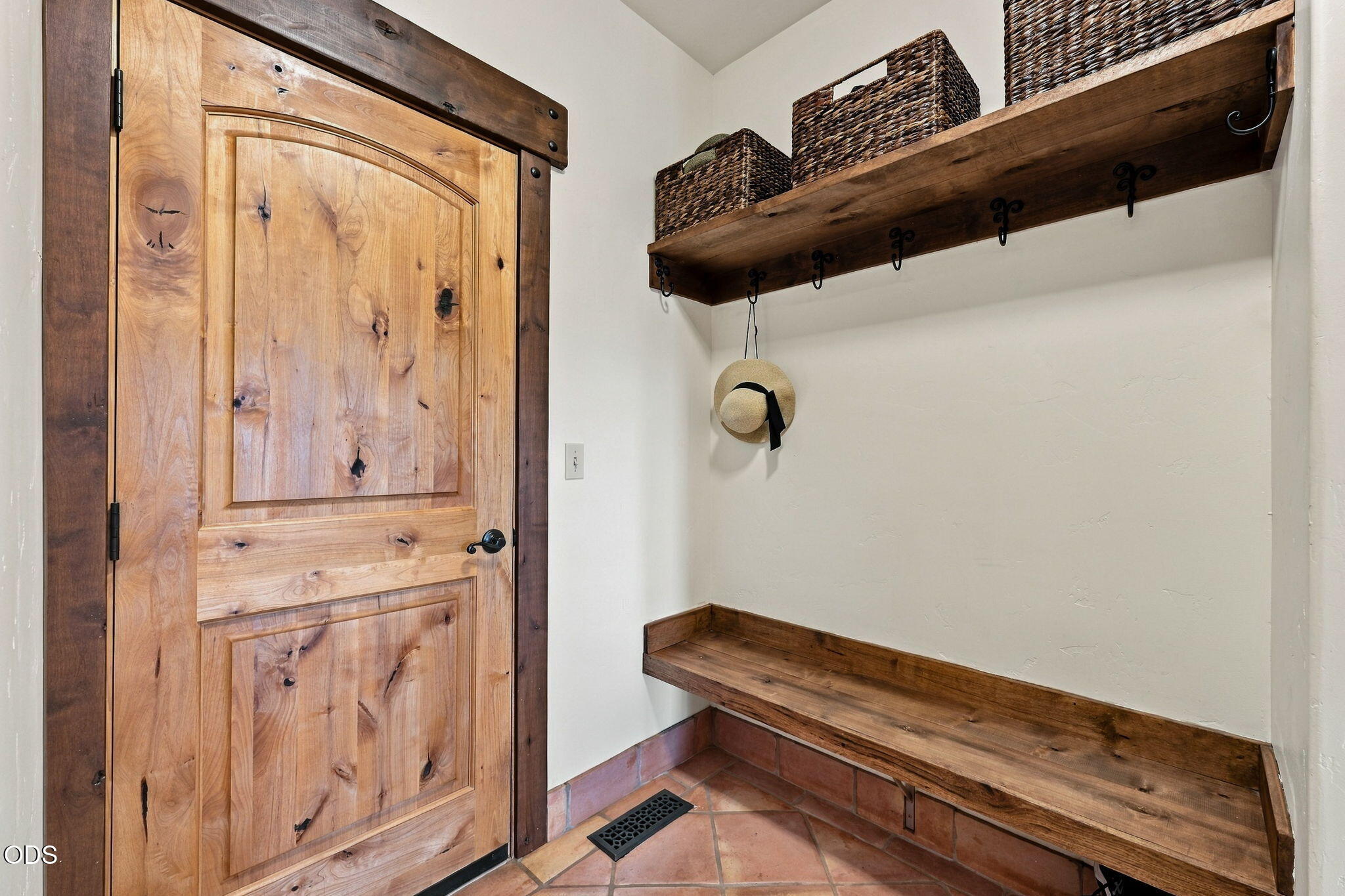 Mudroom with a rustic wood door, built-in bench, overhead shelf, woven baskets, and terracotta tile.