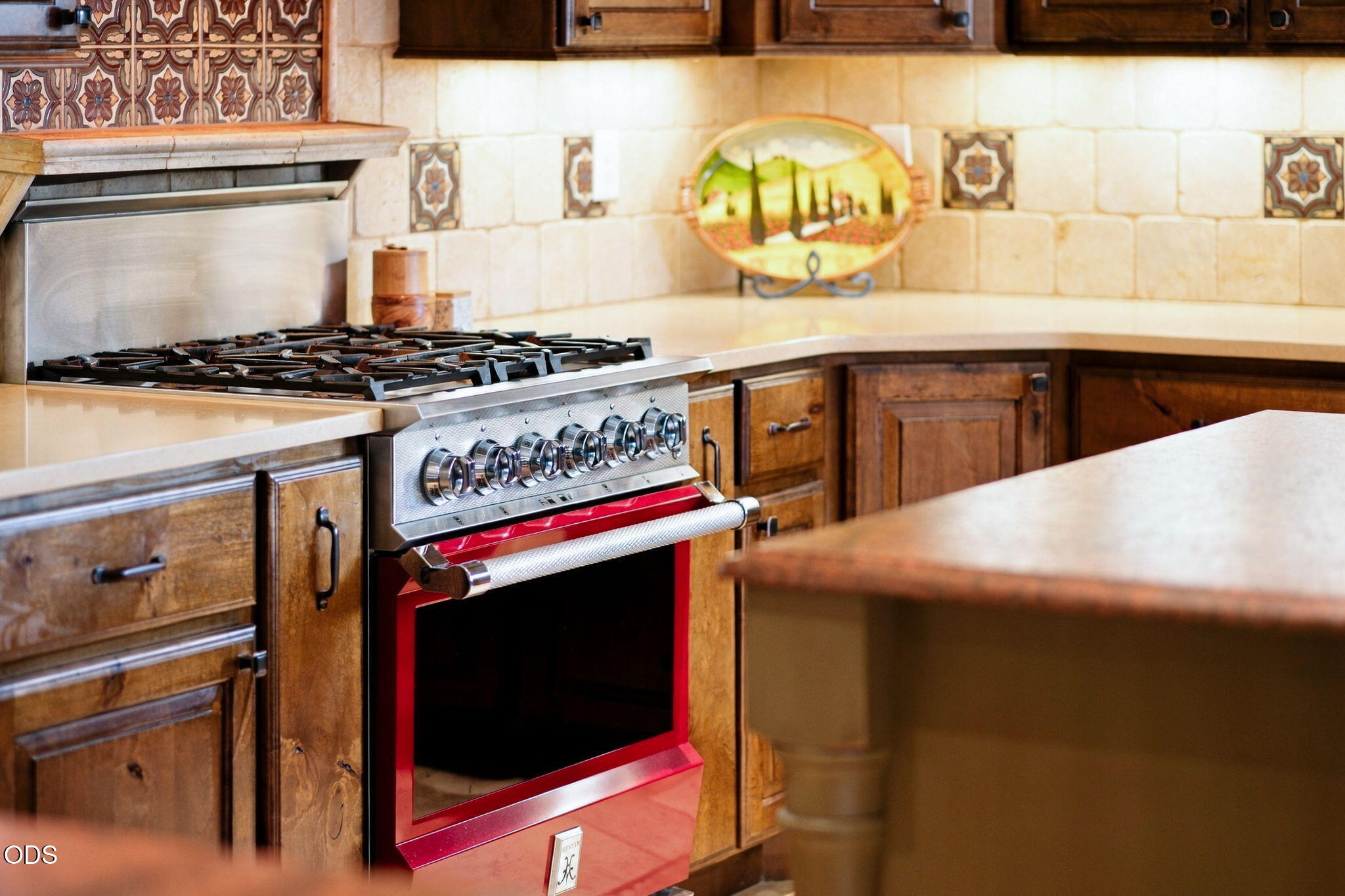 Kitchen with a red-trimmed gas range, rustic wood cabinets, and patterned tile backsplash.