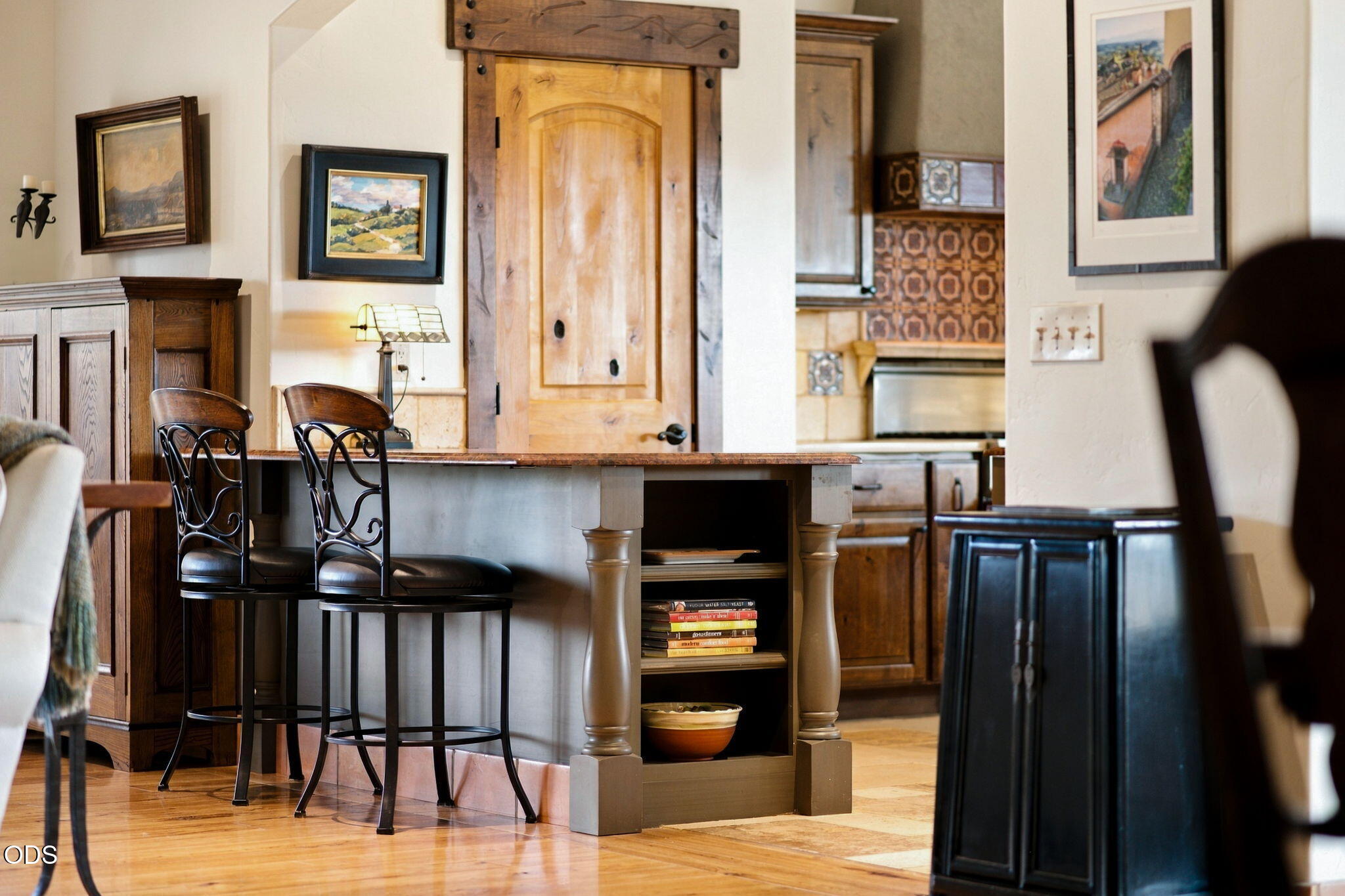 Kitchen with a broad island counter, dark metal stools, wood cabinetry, and a plank-style wooden door.
