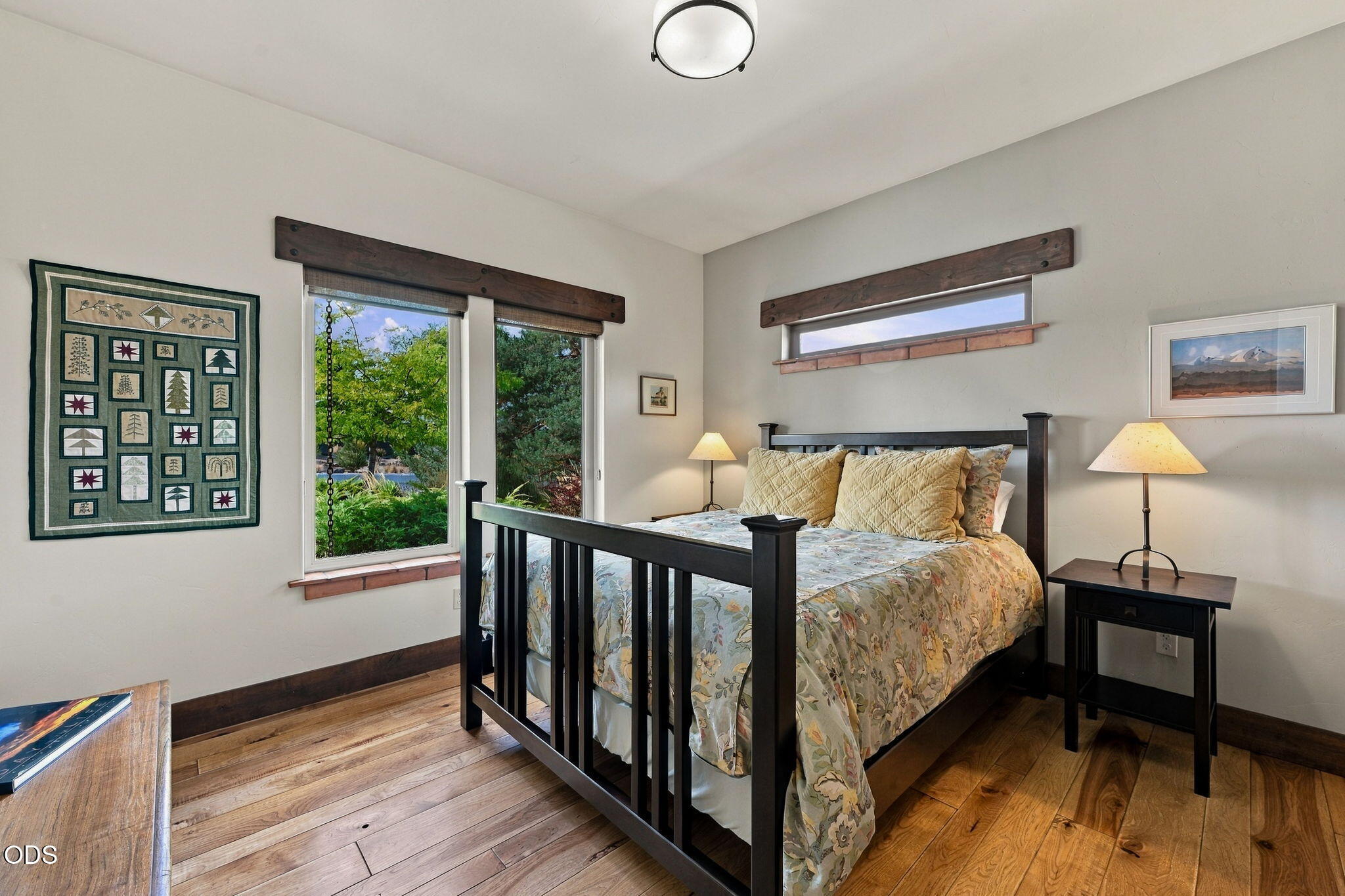 Furnished bedroom with a dark wood four-poster bed, patterned bedding, and windows overlooking greenery.
