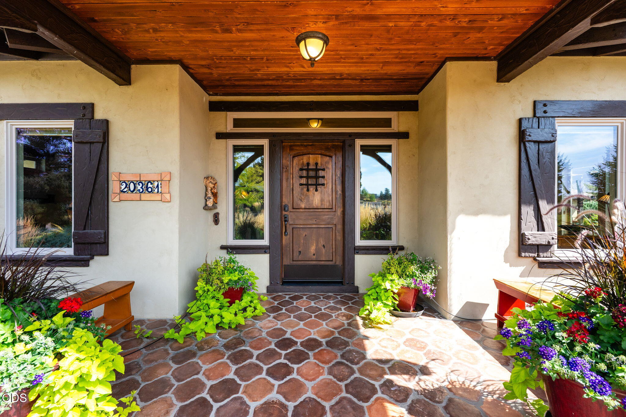 Home’s covered entry with a carved wooden door, stone paving, and colorful flower planters.
