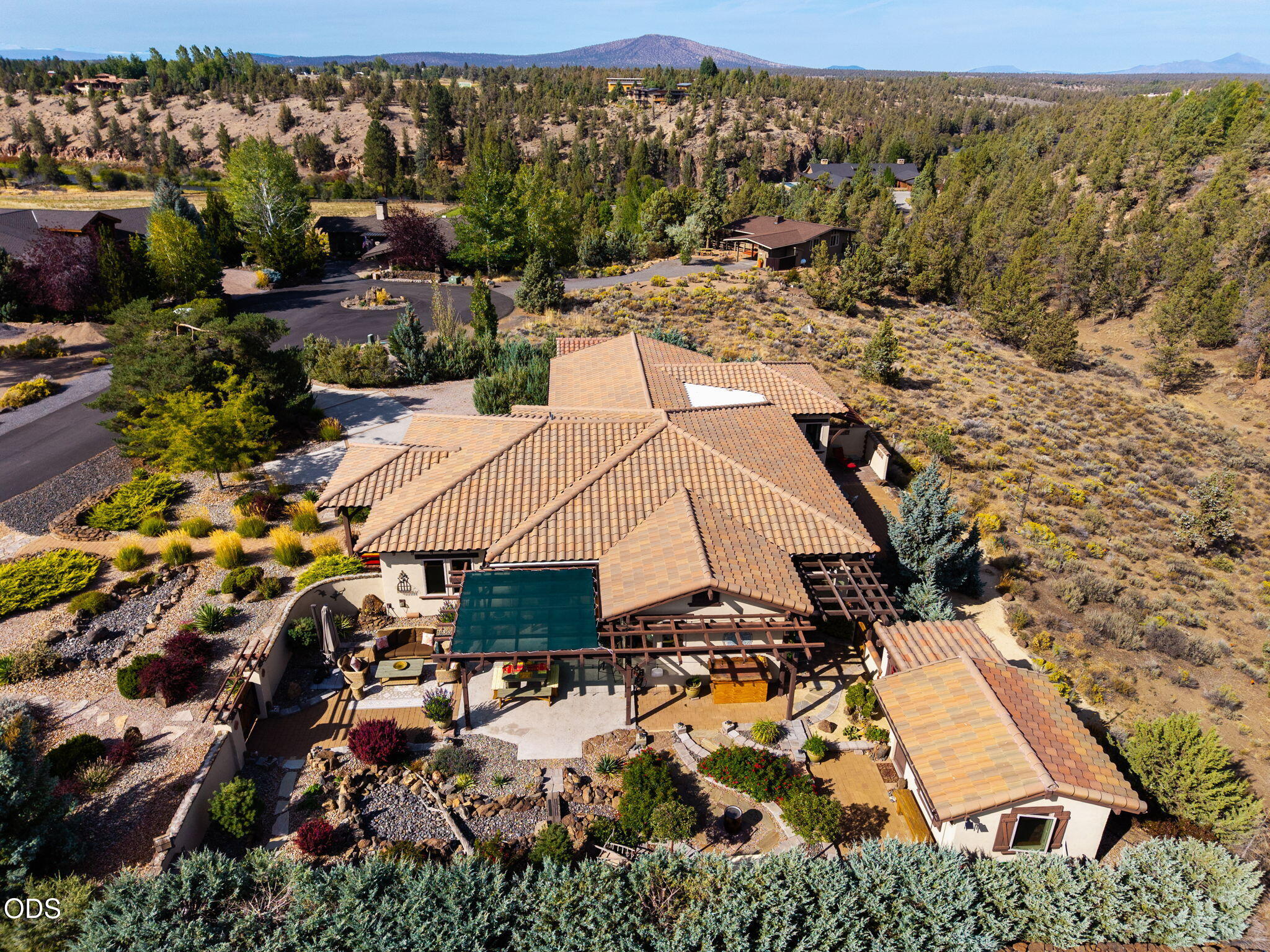 Aerial view of a tile-roofed home with a covered patio, landscaped grounds, and distant mountains.