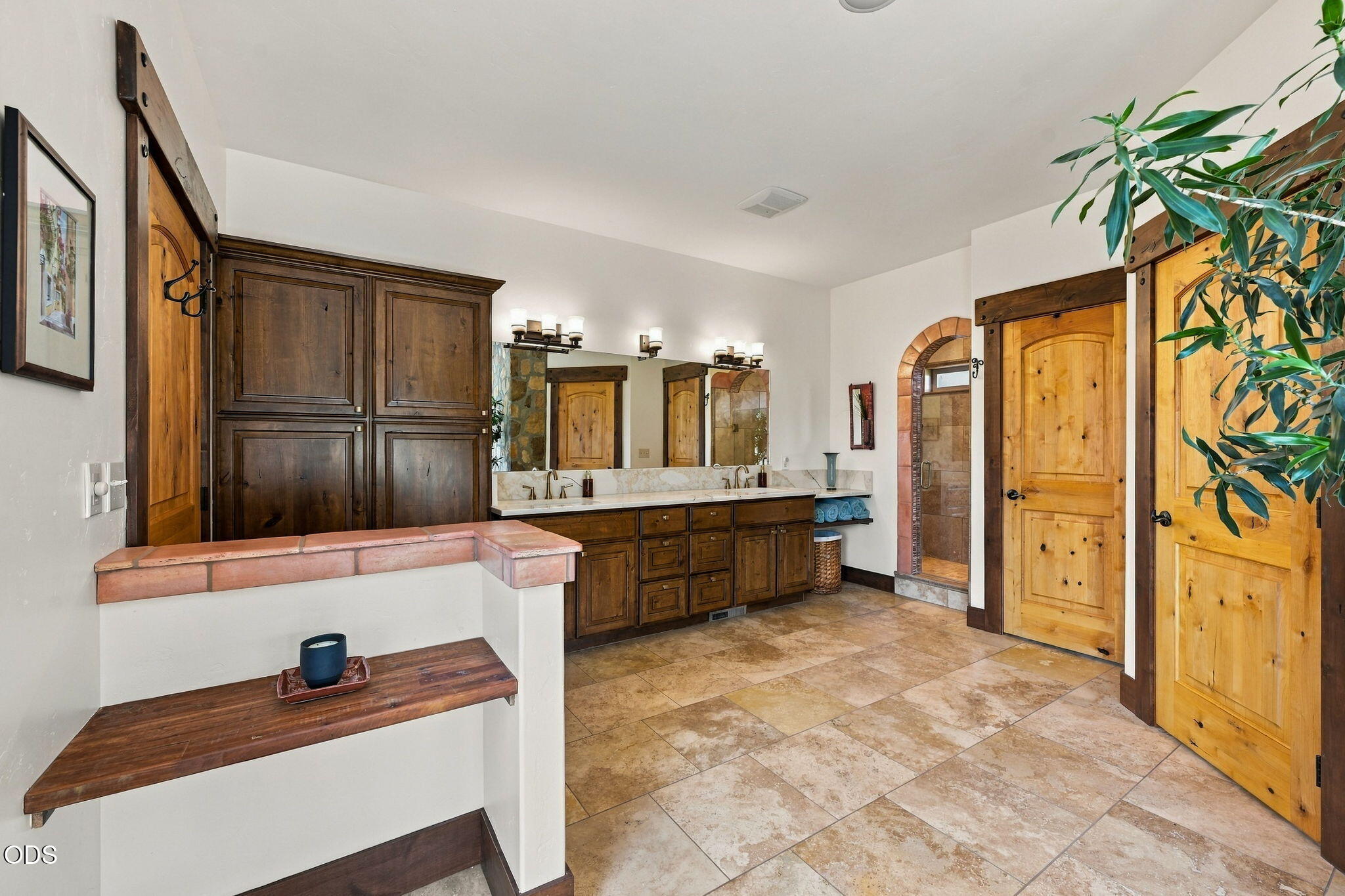 Bathroom with a double-sink dark wood vanity, stone tile floor, and rustic wooden doors.